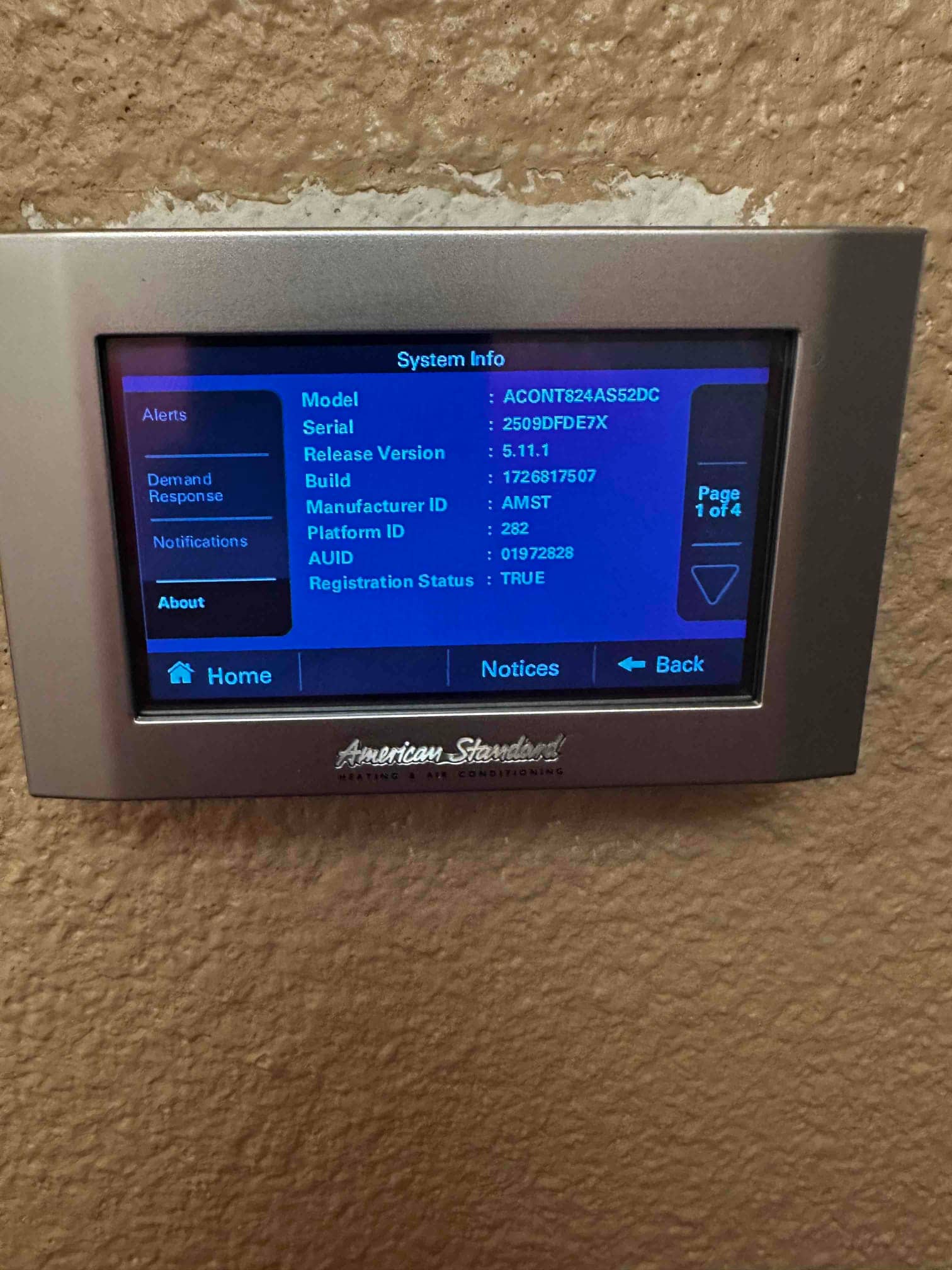 Touchscreen thermostat displays system information menu after installation, mounted on an interior wall with navigation buttons visible.