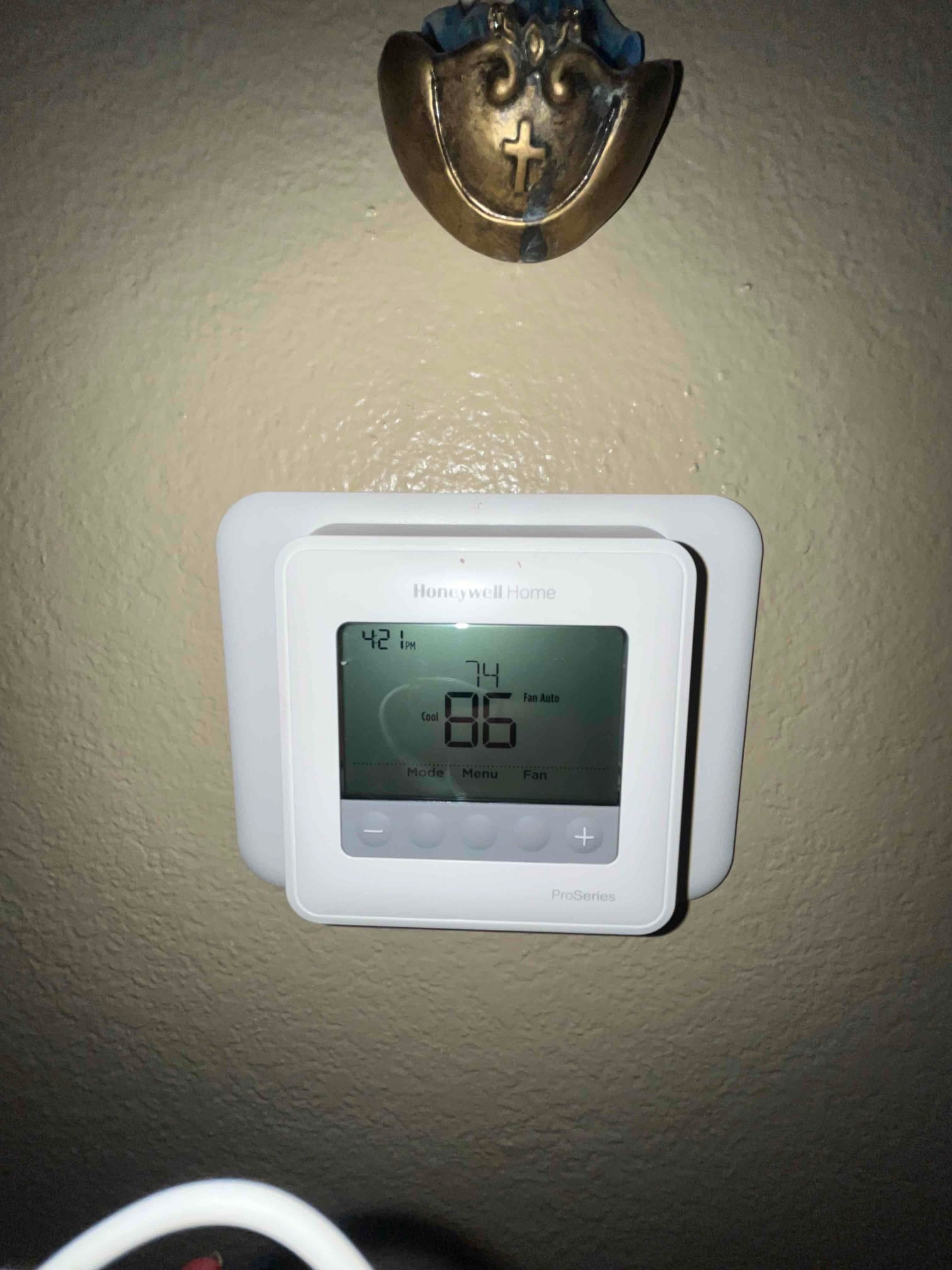 Programmable thermostat on wall displaying 86°F room temperature, 74°F cooling setpoint, and fan set to auto mode.