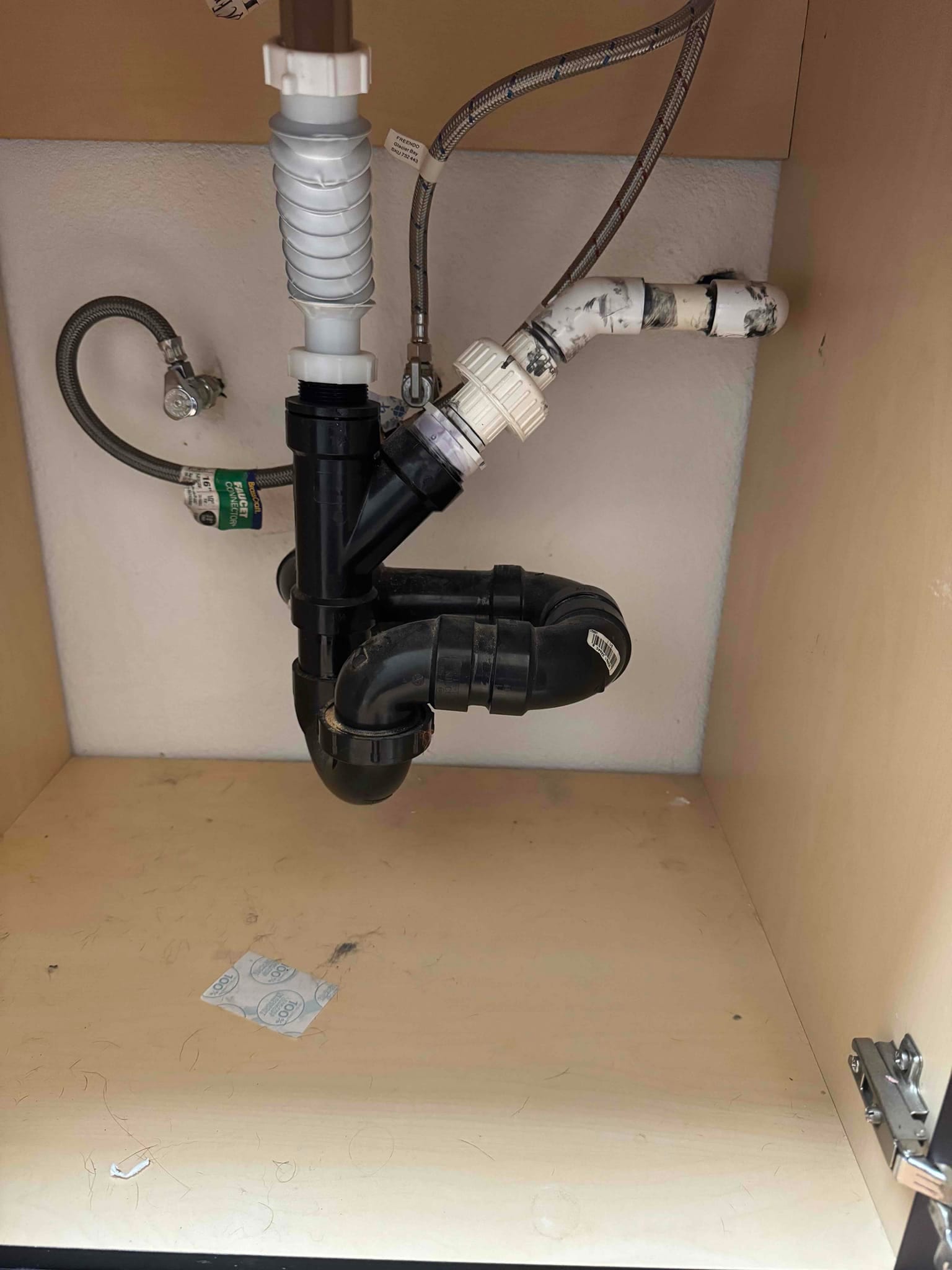PVC condensate drain assembly under a sink, showing P-trap, cleanout, and flexible connections after repair.