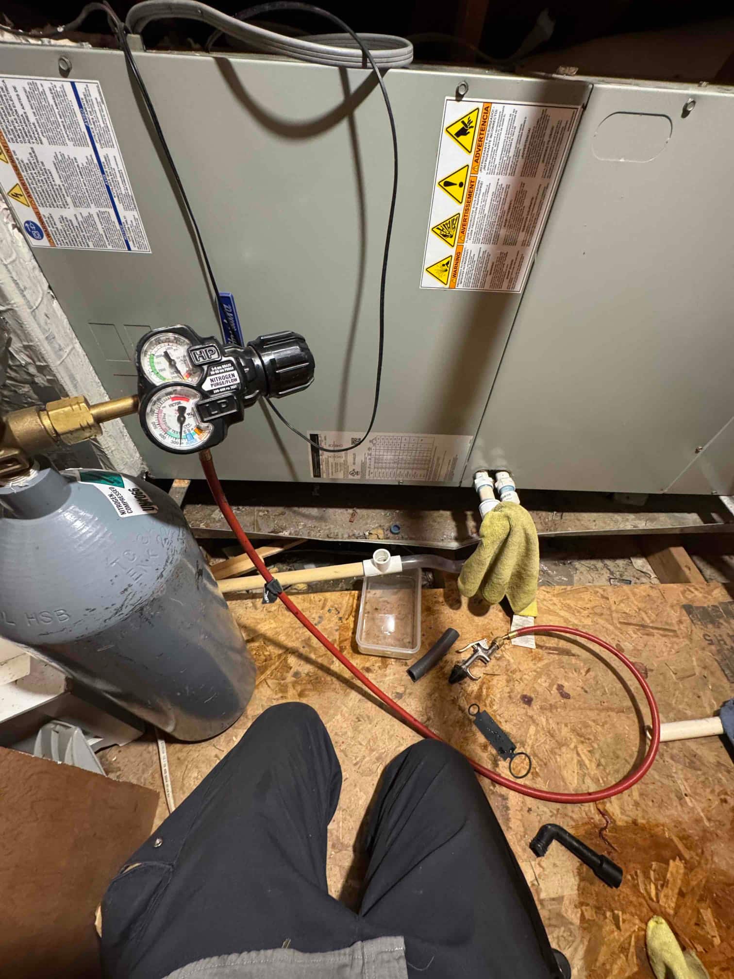 Refrigerant manifold gauges connected to the air handler service ports with hoses attached during system diagnostics and condensate drain cleaning.