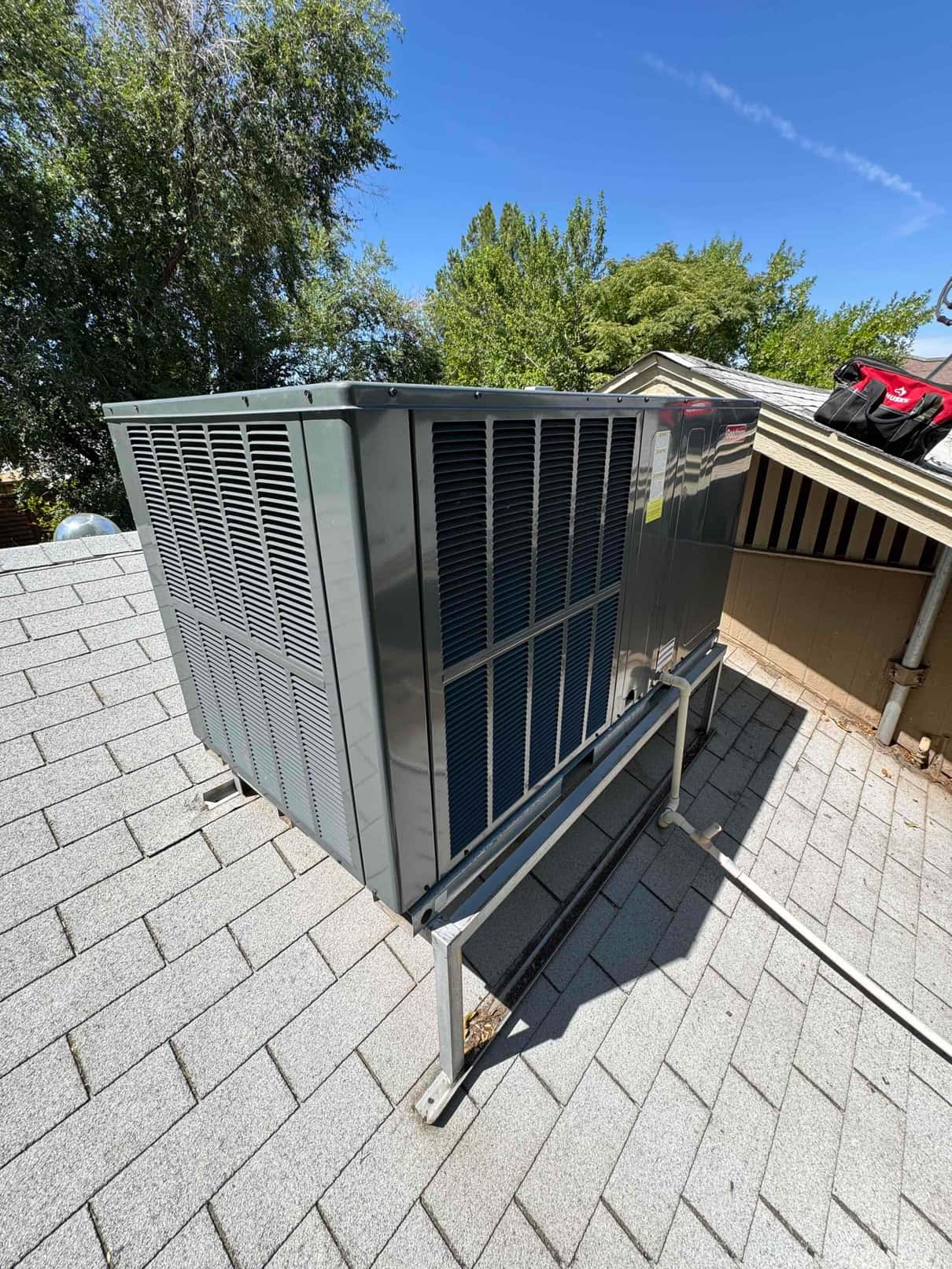 Rooftop air conditioning package unit on a shingle roof with curb stand and side ventilation panels visible.