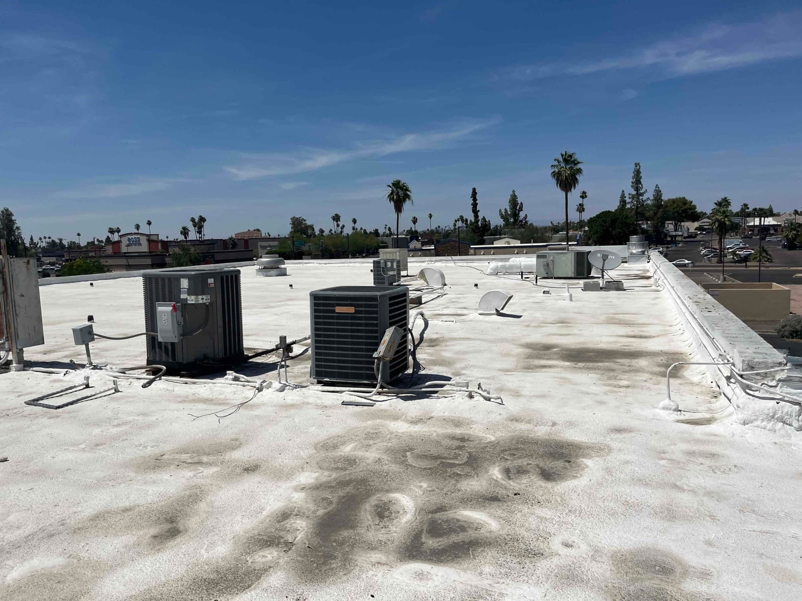 Rooftop with multiple air conditioning condenser units and refrigerant lines, showing weathered surfaces and scattered rooftop equipment under clear skies.
