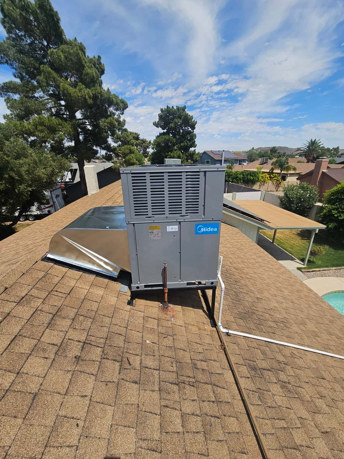 Rooftop package heat pump installed on a curb with new drain line and sealed roof penetration, viewed from above.