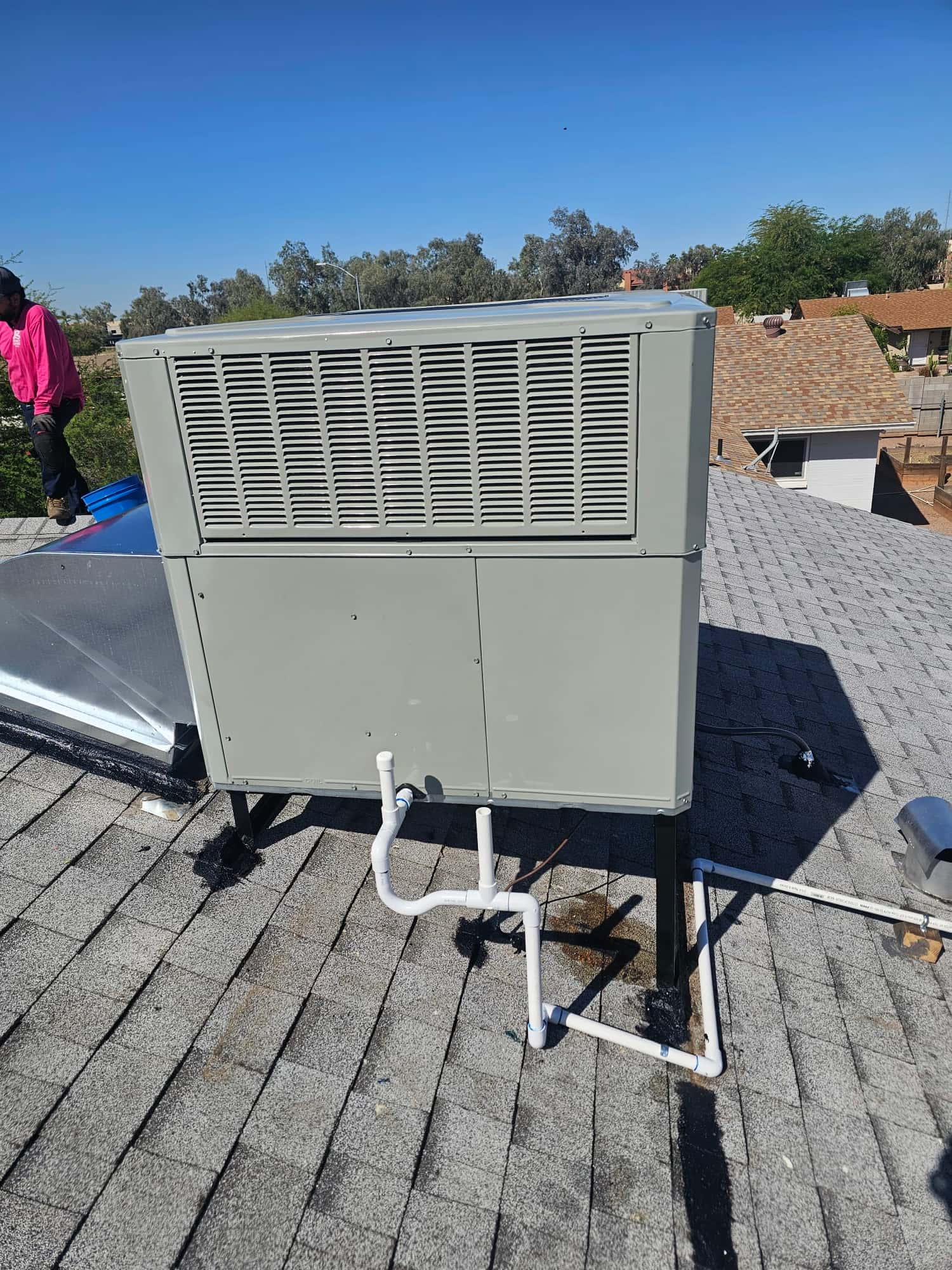 Rooftop package HVAC unit installed on stands with new condensate drain piping routed across the shingles.