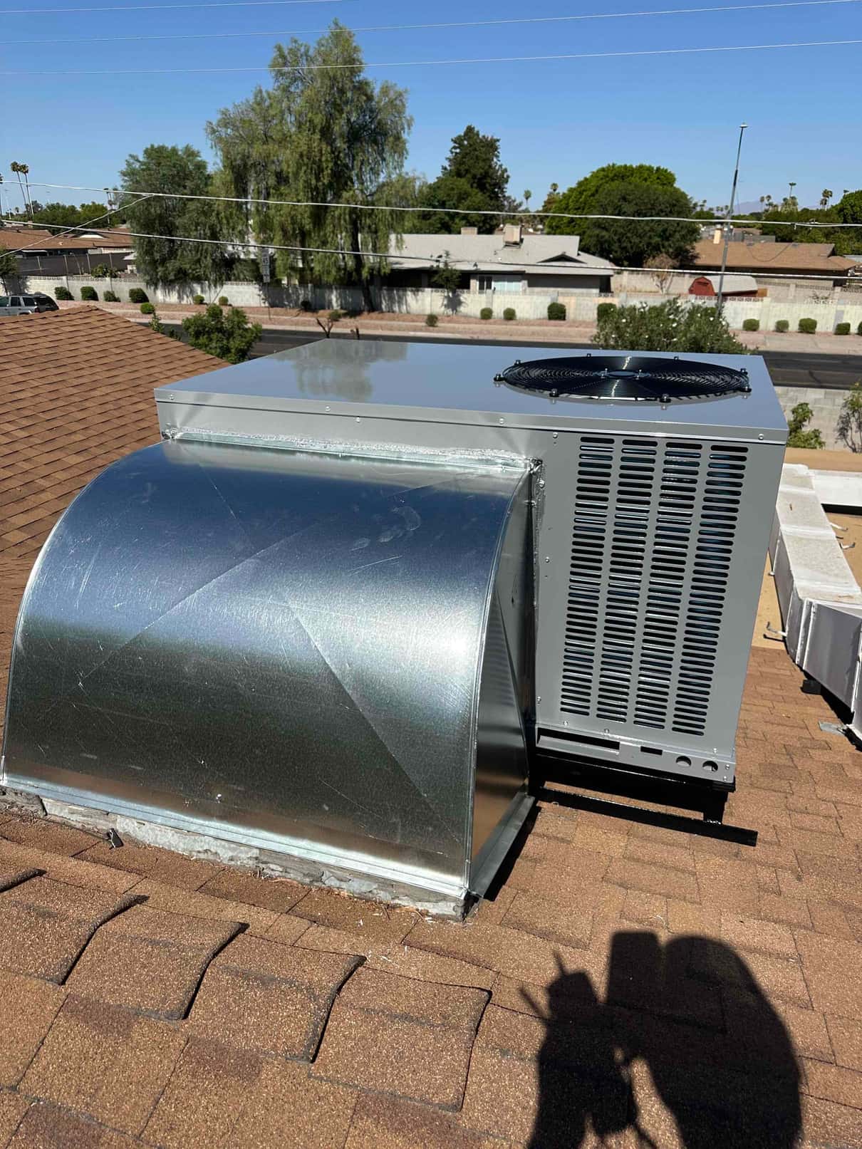 Rooftop package HVAC unit set and connected to new sheet-metal curb and duct transition on shingle roof.