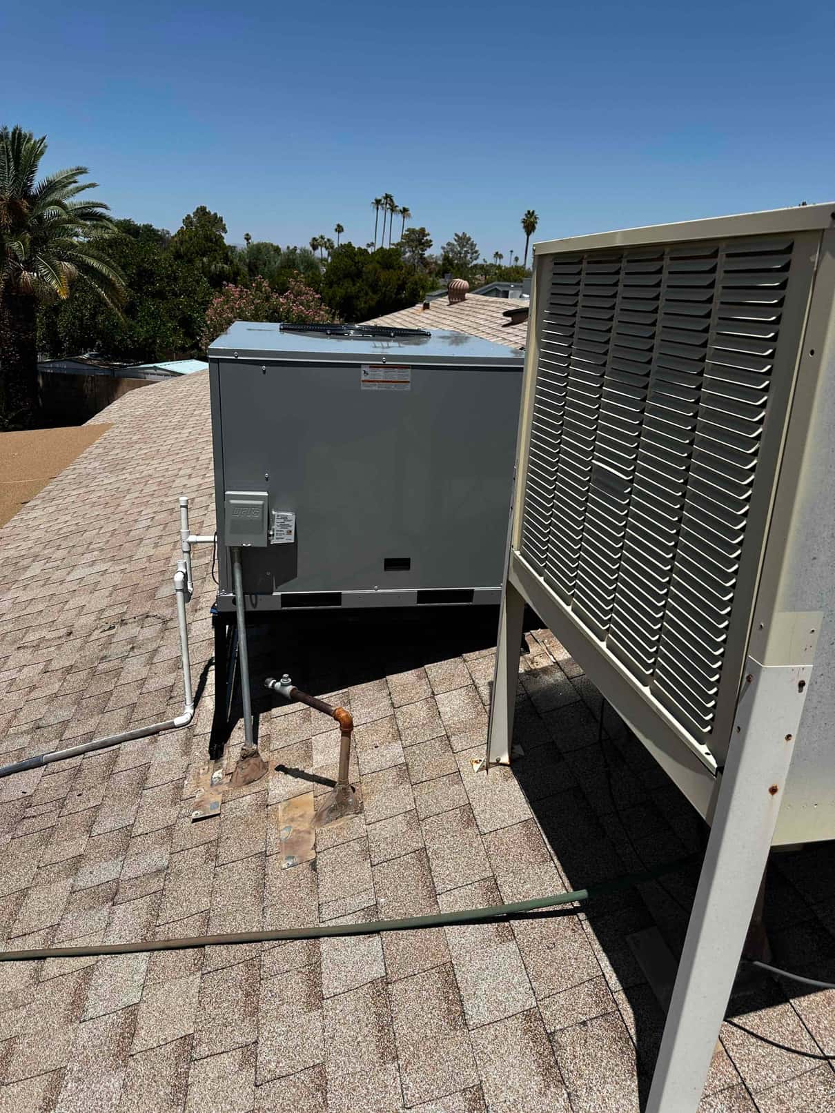 Rooftop package unit installed on shingles with new electrical disconnect and condensate drain routing visible beside the cabinet.