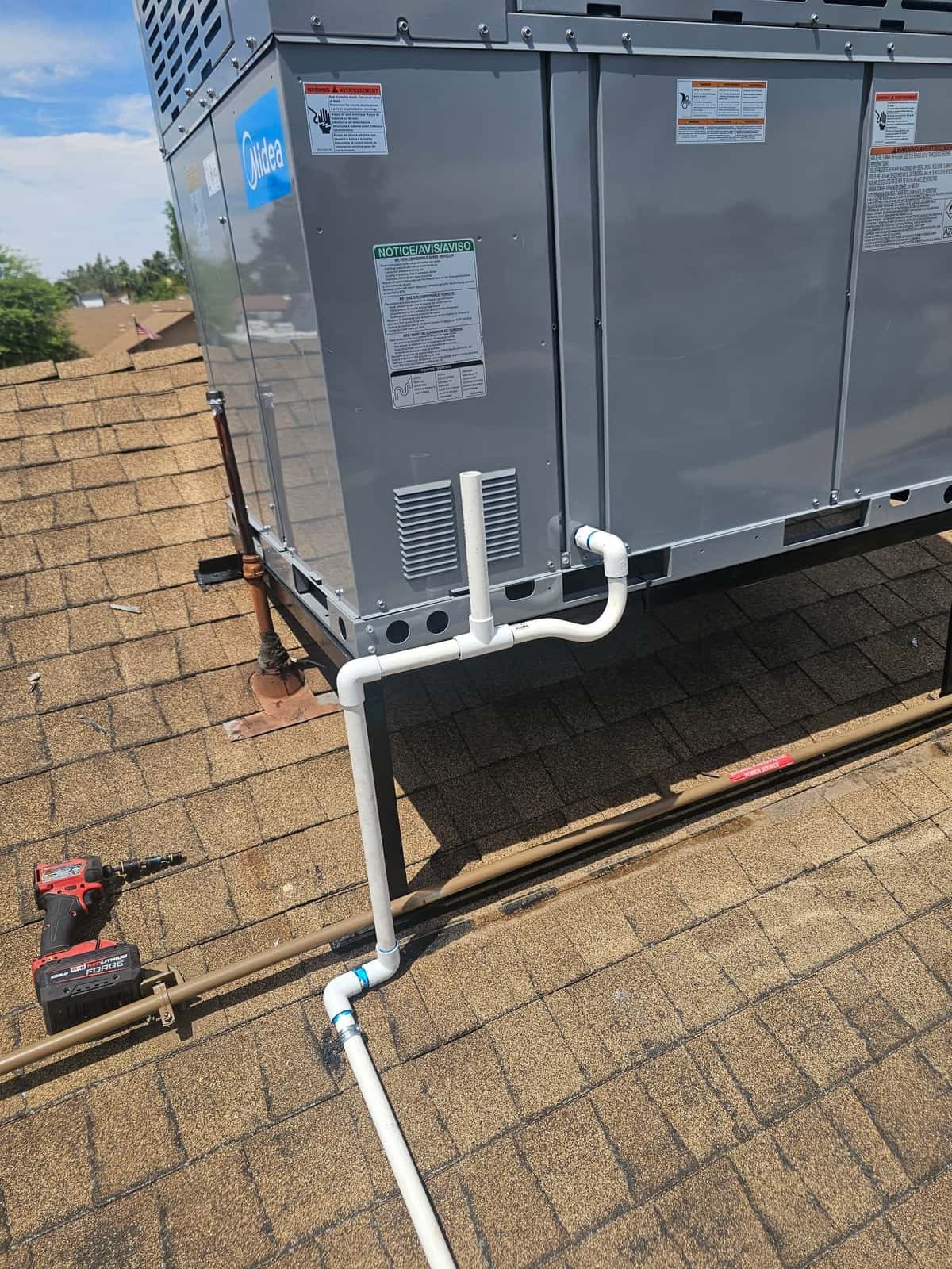 Rooftop packaged unit installed with newly plumbed condensate drain piping and insulated refrigerant line set routing on the shingle roof.