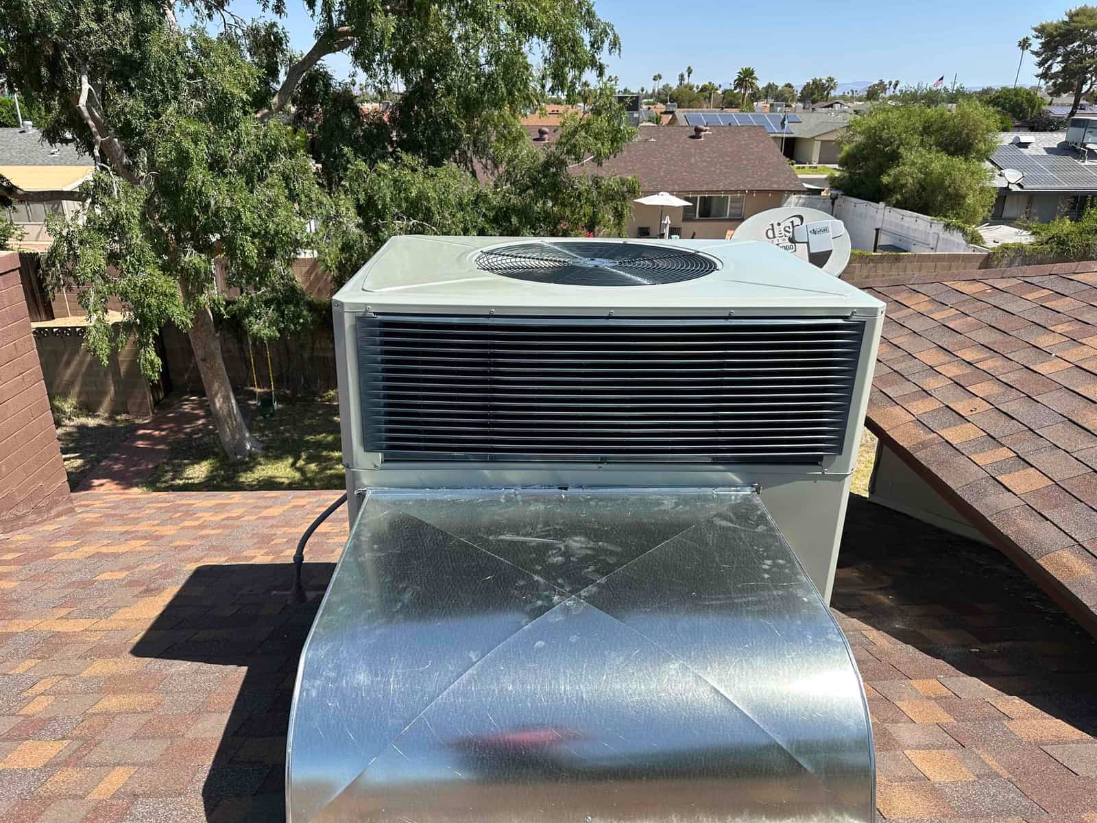 Rooftop 5-ton package unit installed with new galvanized supply plenum connected, set on shingle roof under clear sky.
