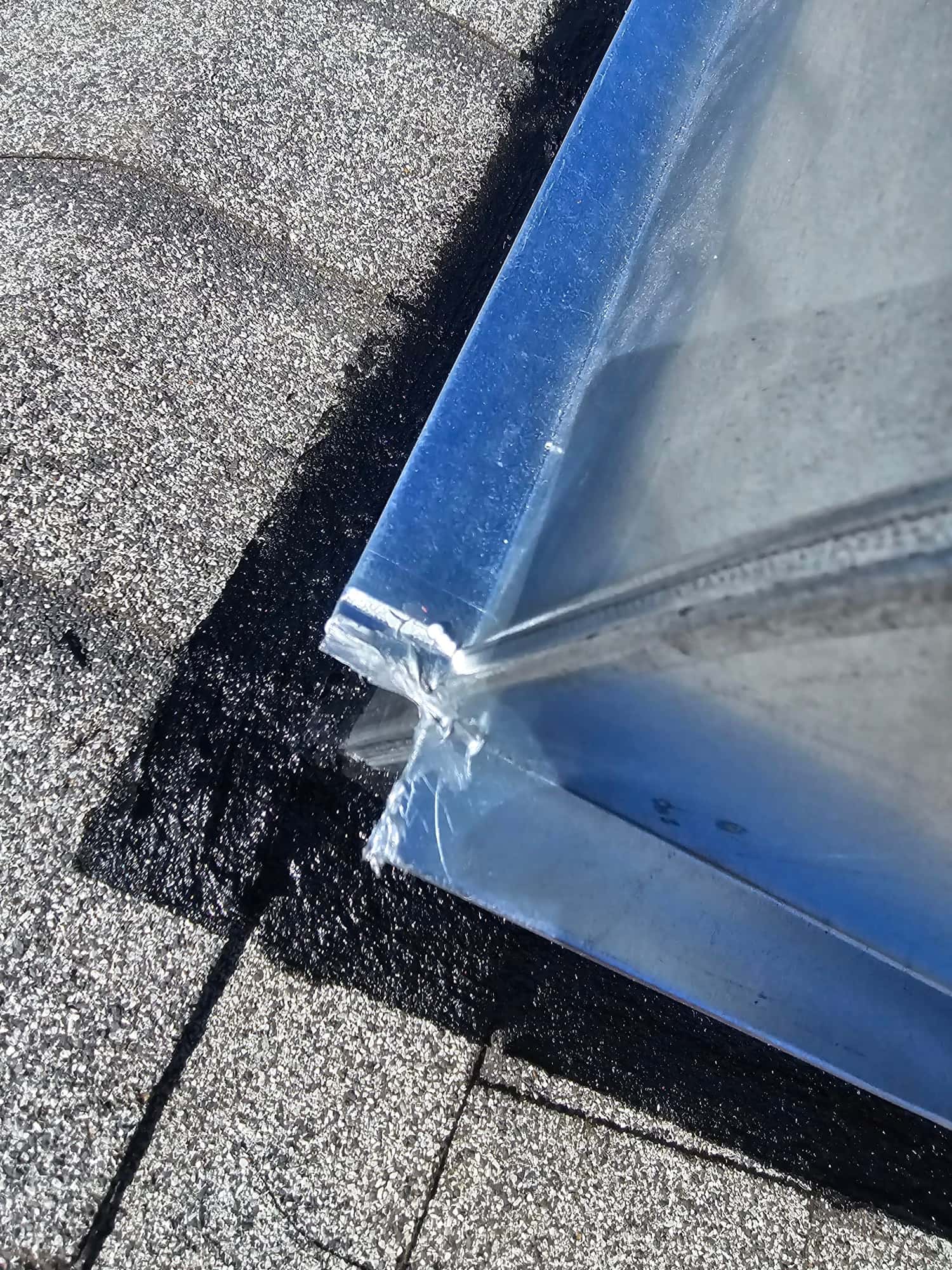Sheet metal curb flashing set on a shingle roof with mastic applied at the perimeter for weather sealing.
