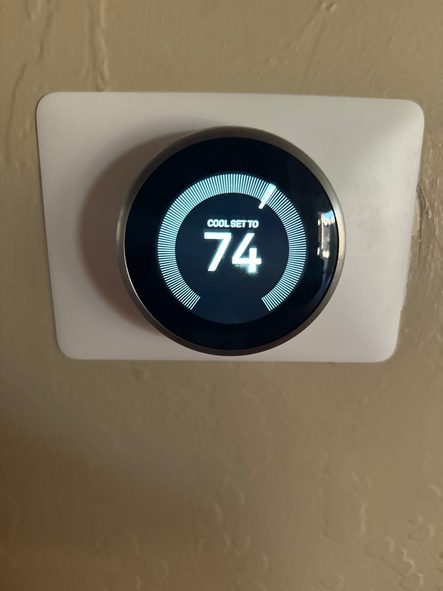 Smart thermostat display shows cooling mode set to 74 degrees, mounted on a wall with a trim plate.