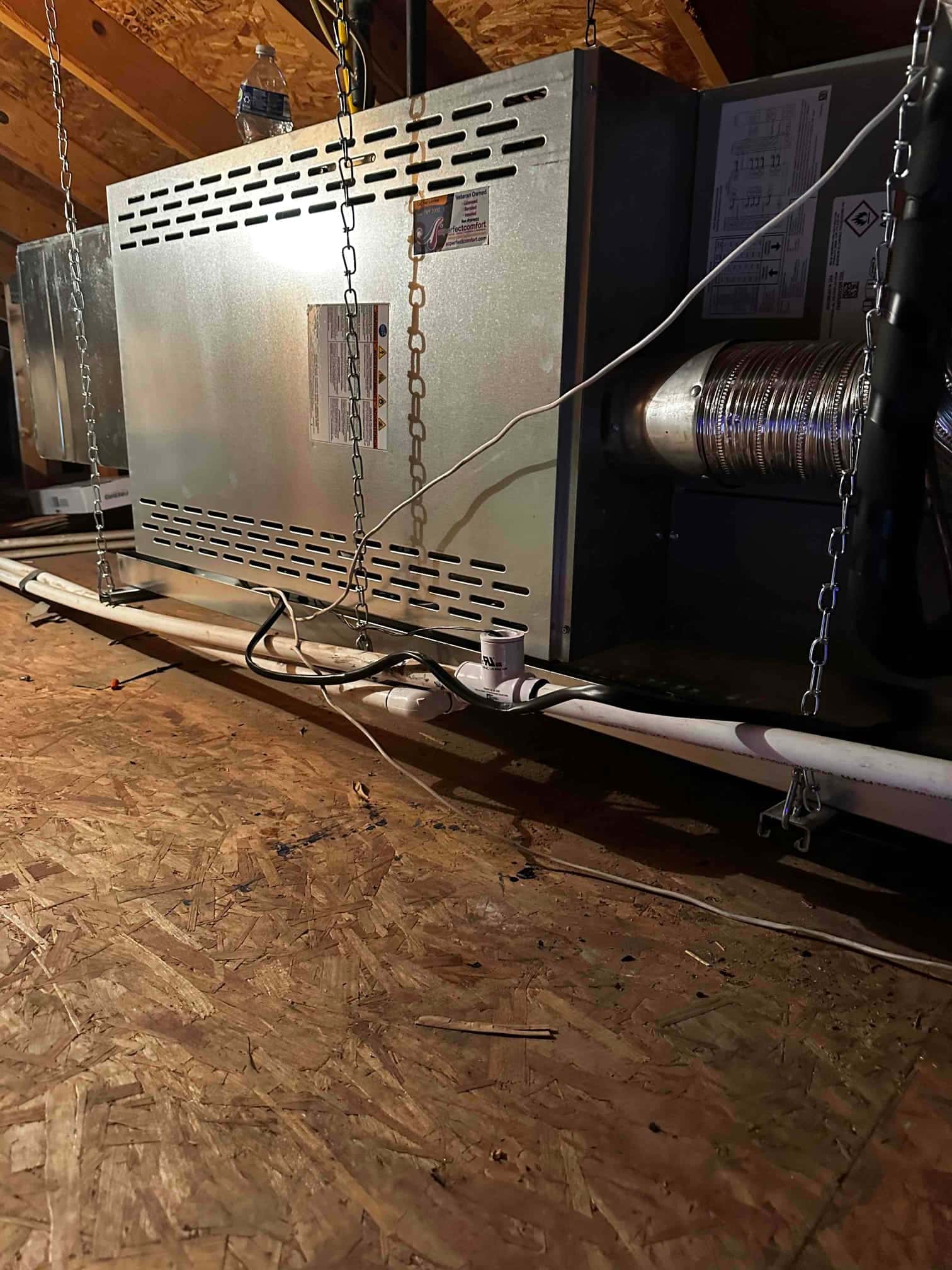 Suspended horizontal air handler installed in attic with insulated duct connection and PVC condensate drain with float switch.