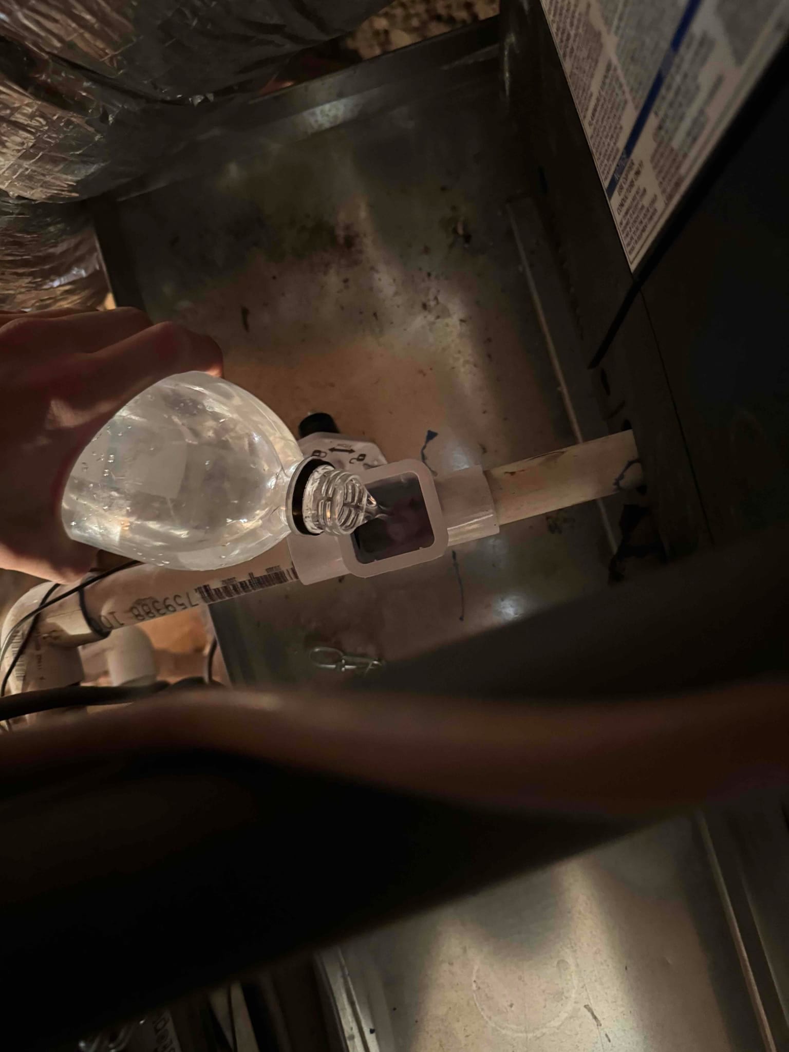 Technician flushes the condensate drain line with a squeeze bottle connected to a cleanout fitting on the PVC trap.