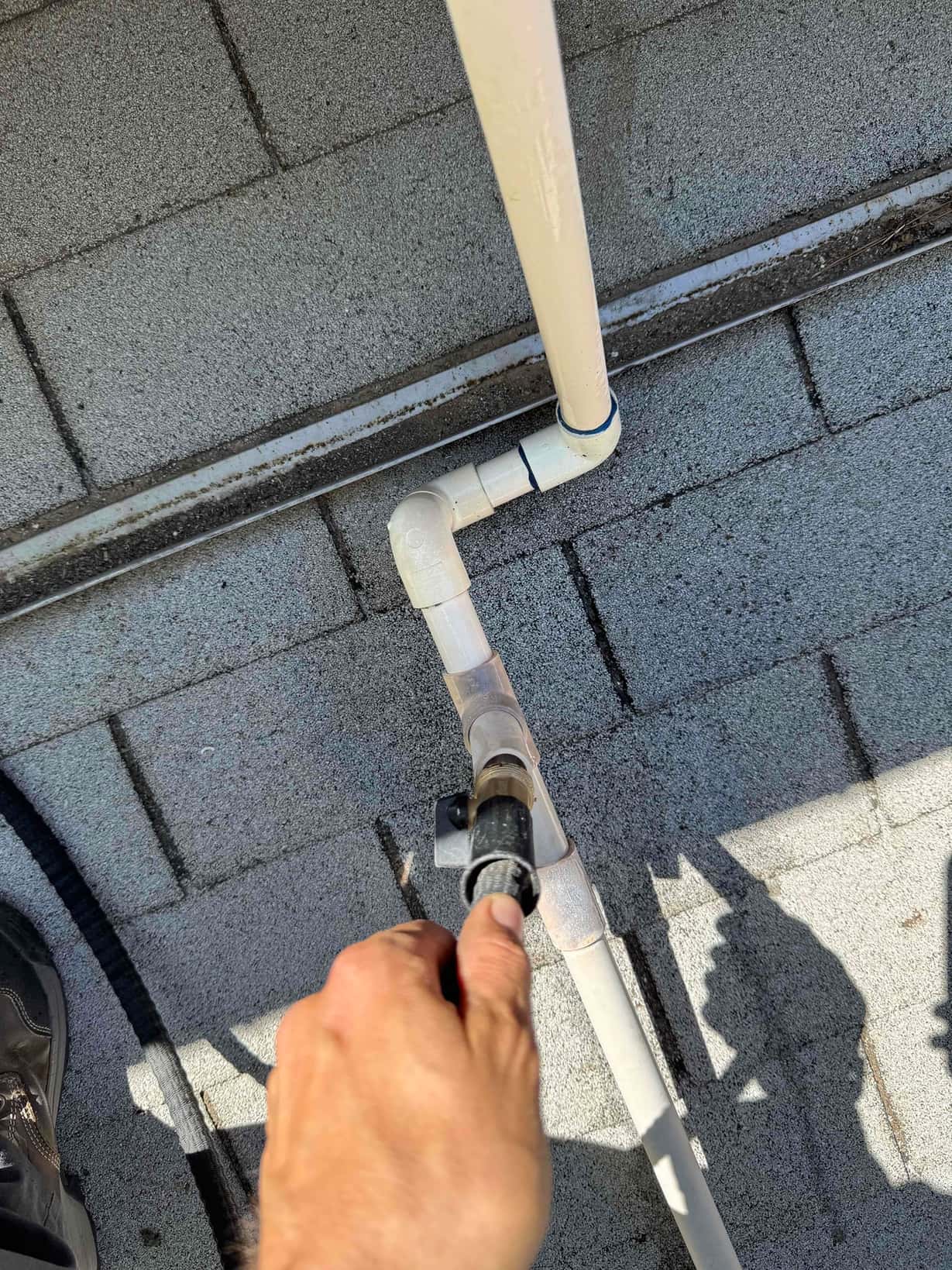 Technician’s hand holds a shop vacuum hose at a PVC condensate drain cleanout on a rooftop air conditioning system.