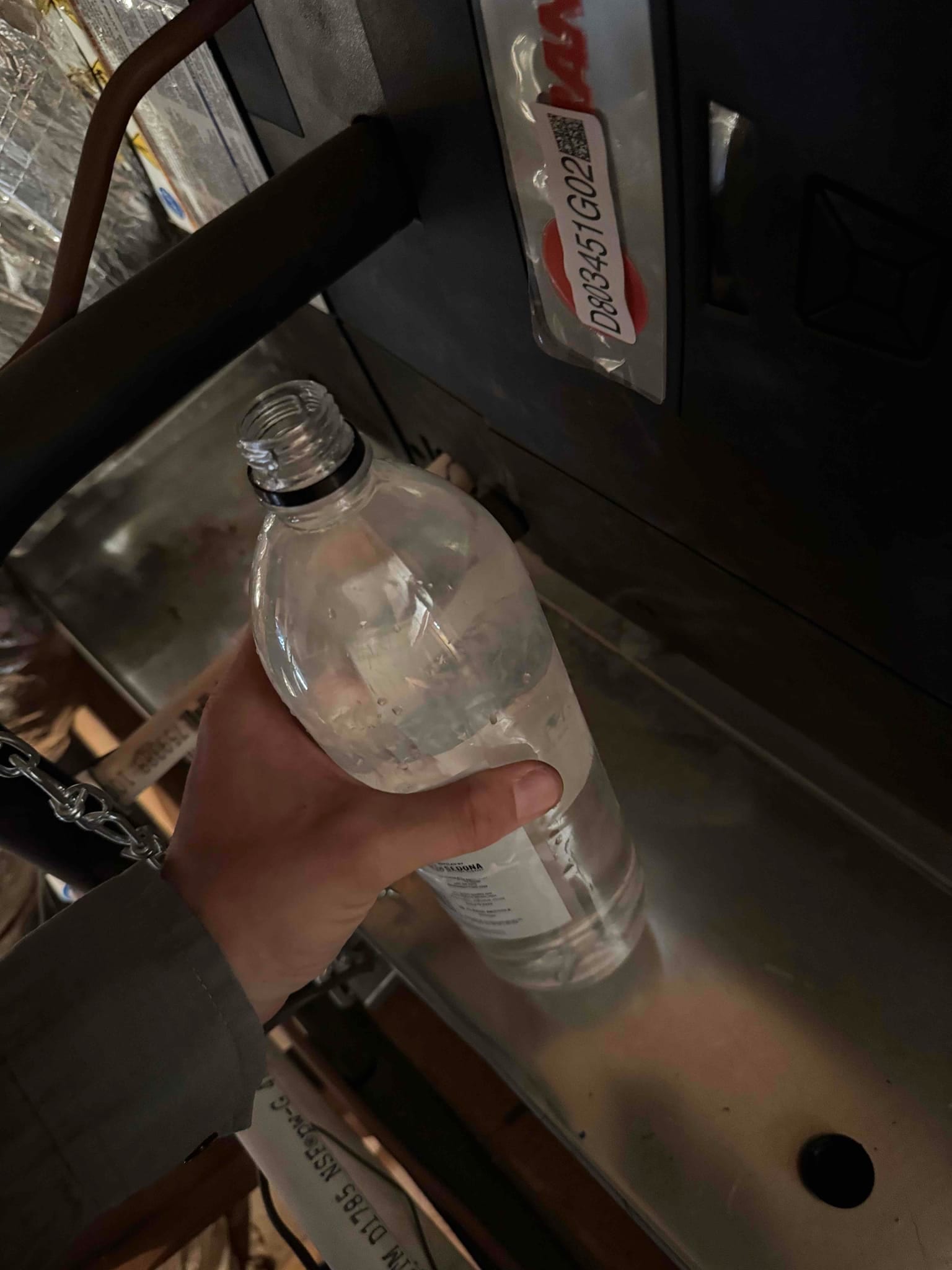 Technician’s hand pours water from a bottle into an air handler’s condensate drain pan to check drain line flow.