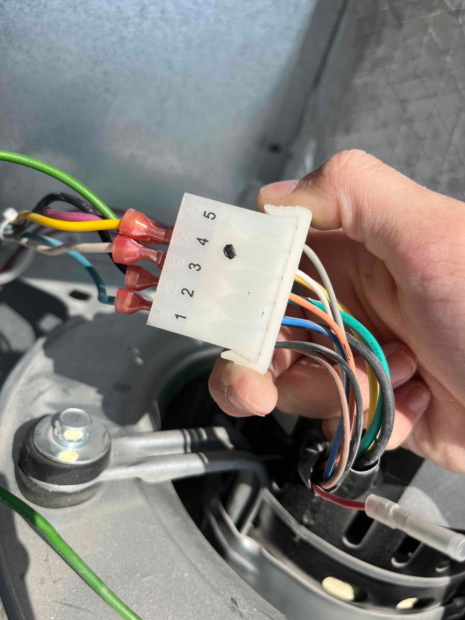 Technician holds indoor blower motor wiring connector with numbered positions and multiple colored leads visible at the air handler.