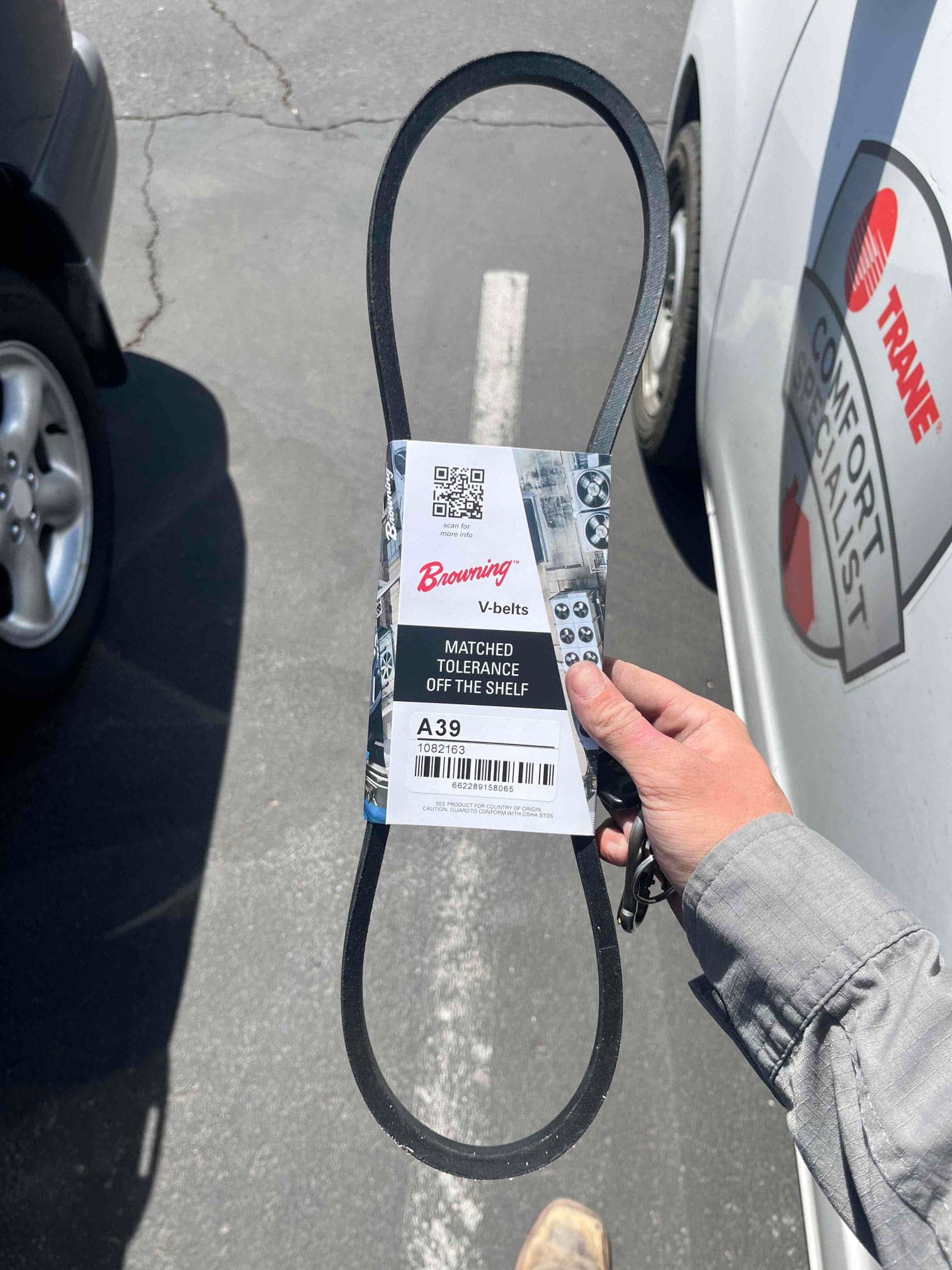 Technician holds a new Browning A39 V-belt for HVAC drive replacement in the outdoor parking area.