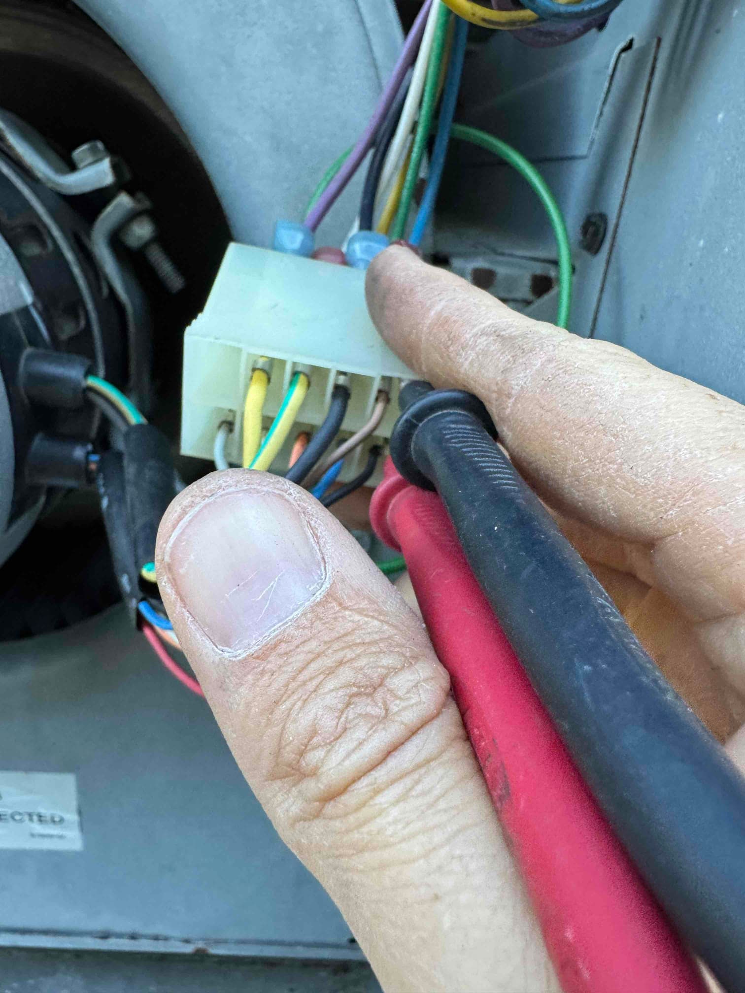 Technician holds probe leads at a blower motor wiring connector inside the air handler during blower motor replacement.