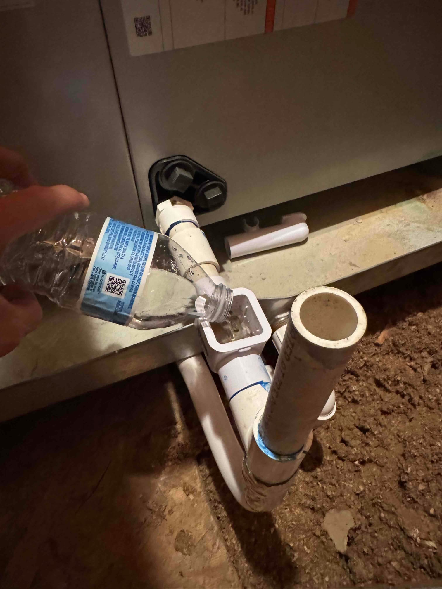 Technician pours water into an air handler condensate drain cleanout to verify flow after cleaning the PVC drain line.