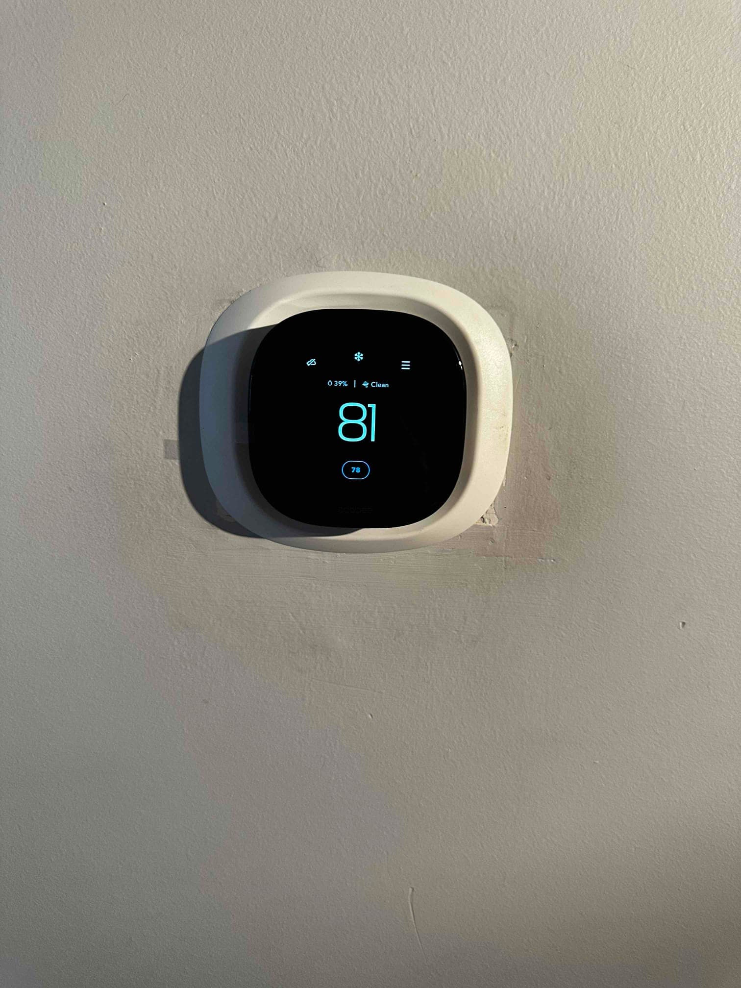 Wall-mounted digital thermostat installed with display illuminated and setpoint visible, confirming control interface placement after system installation.