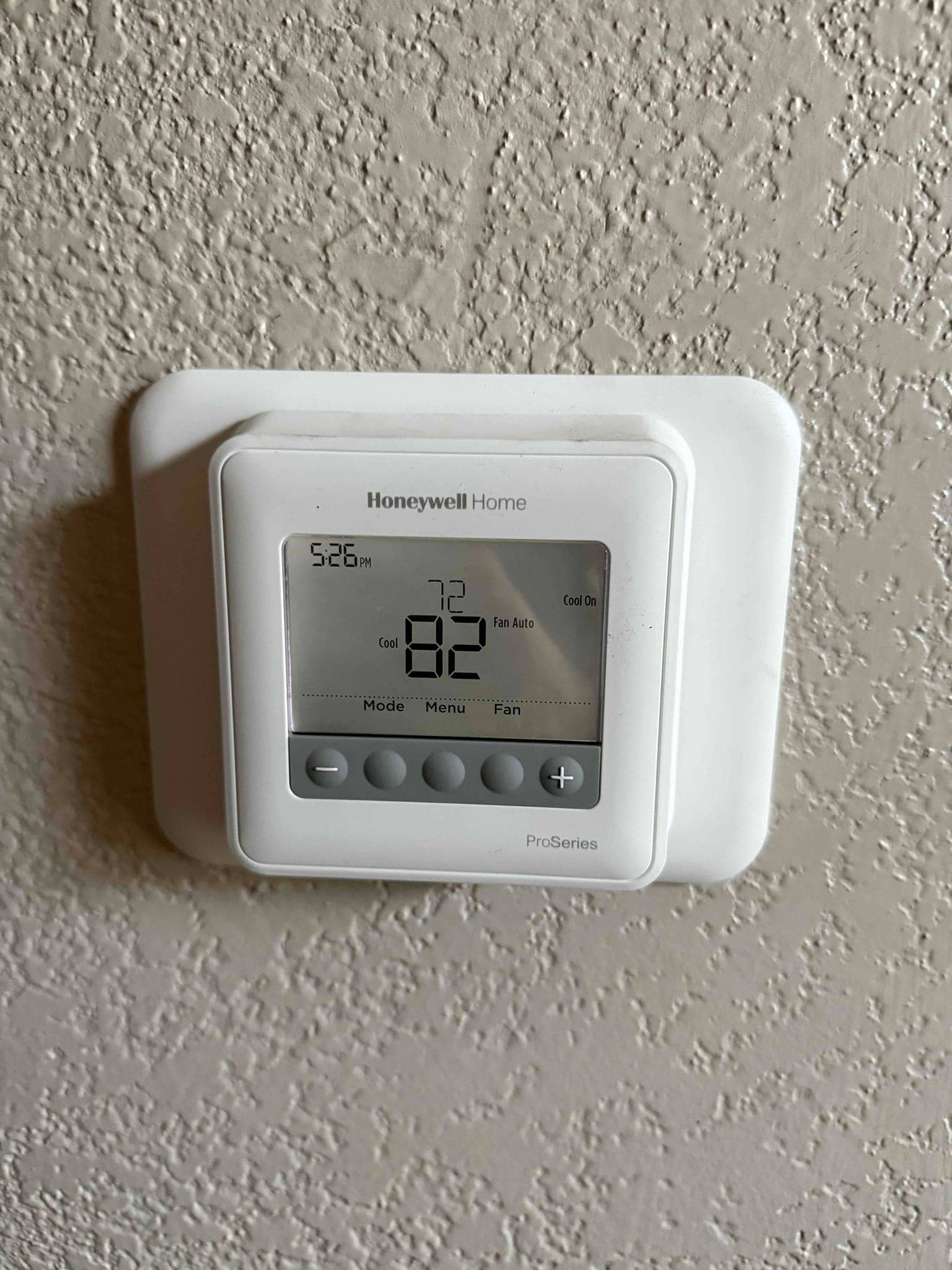 Wall-mounted digital thermostat installed and powered, displaying cooling mode with current room temperature shown on the screen.