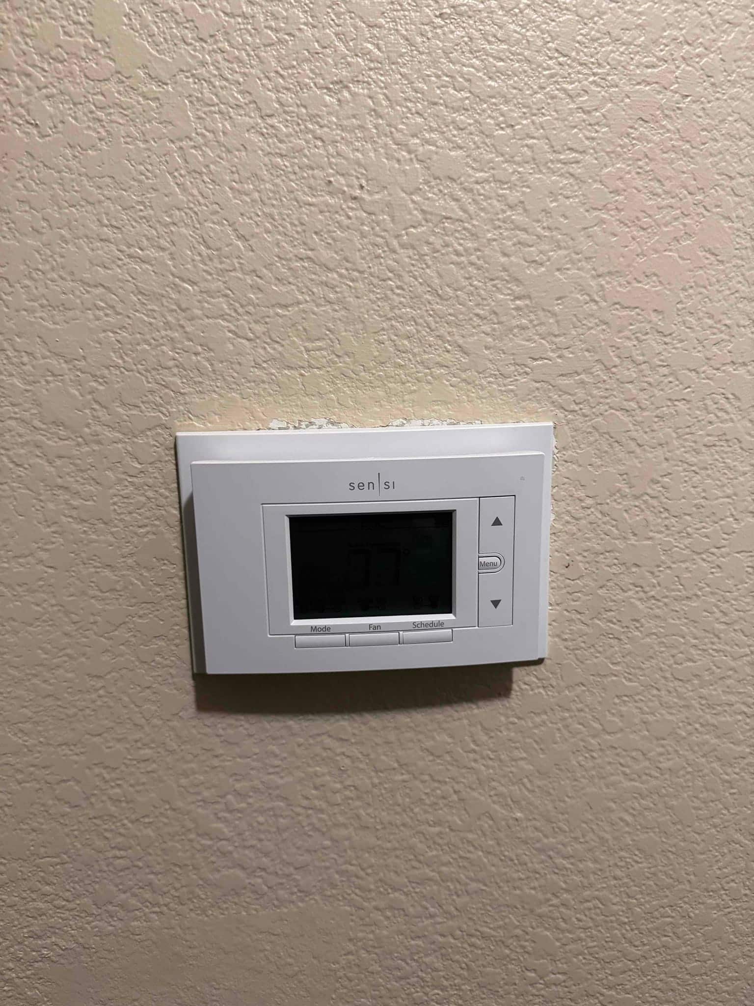Wall-mounted digital thermostat with screen on and control buttons visible, showing system control at the repair site.