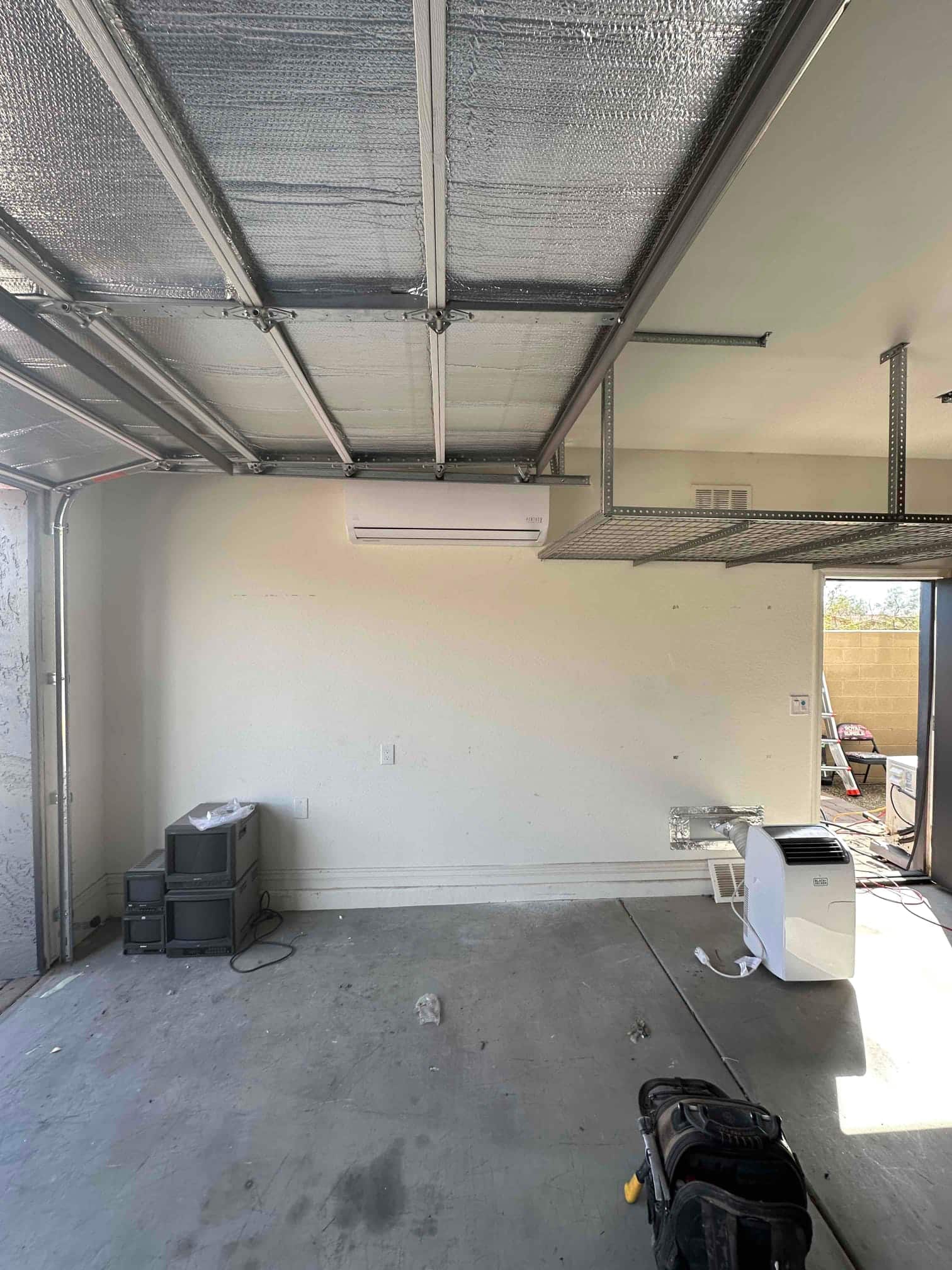 Wall-mounted mini-split indoor unit installed in a garage, with line set penetration and surrounding workspace visible.