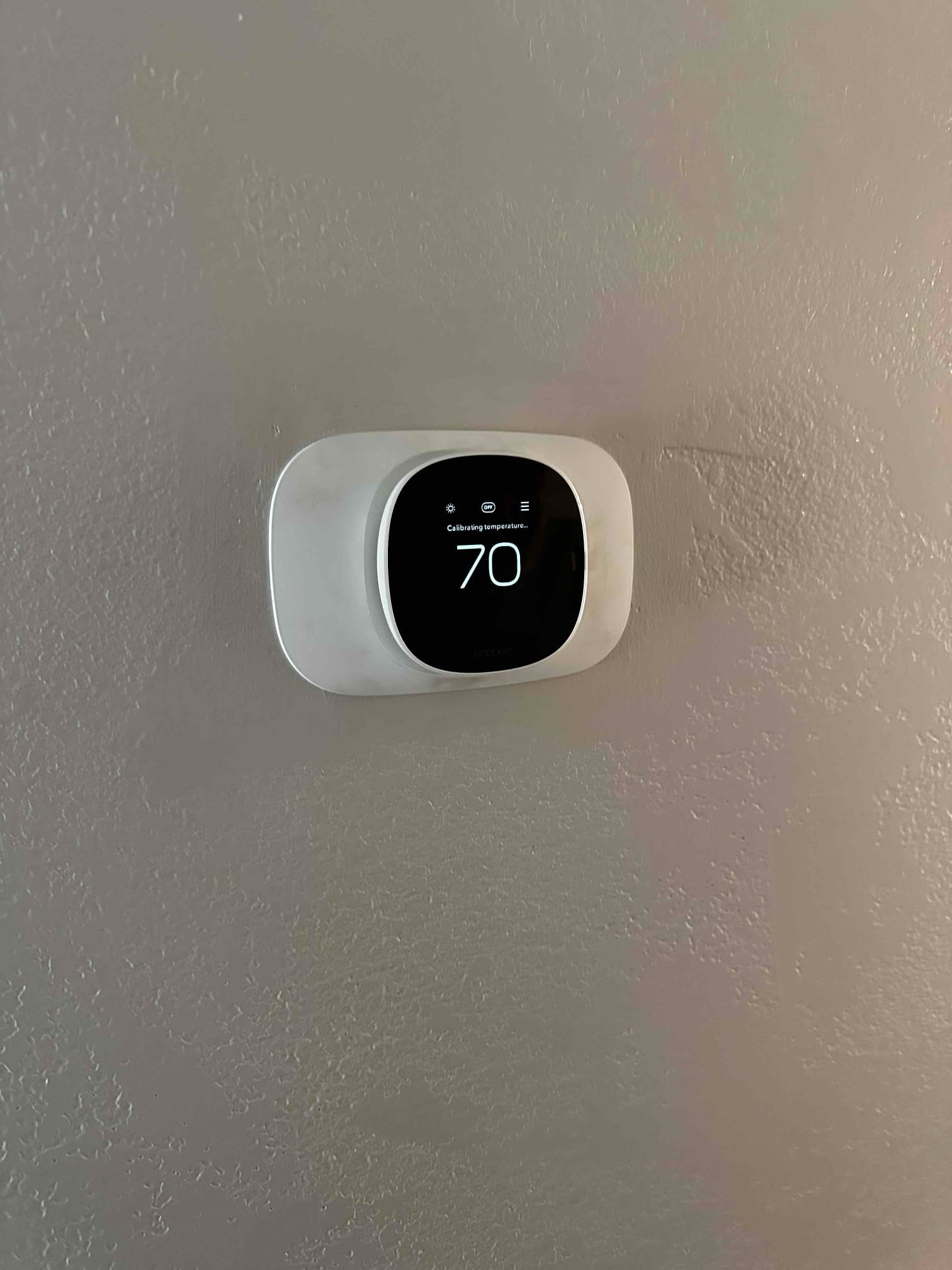 Wall-mounted smart thermostat displays 70 degrees and shows a calibration status after installation.
