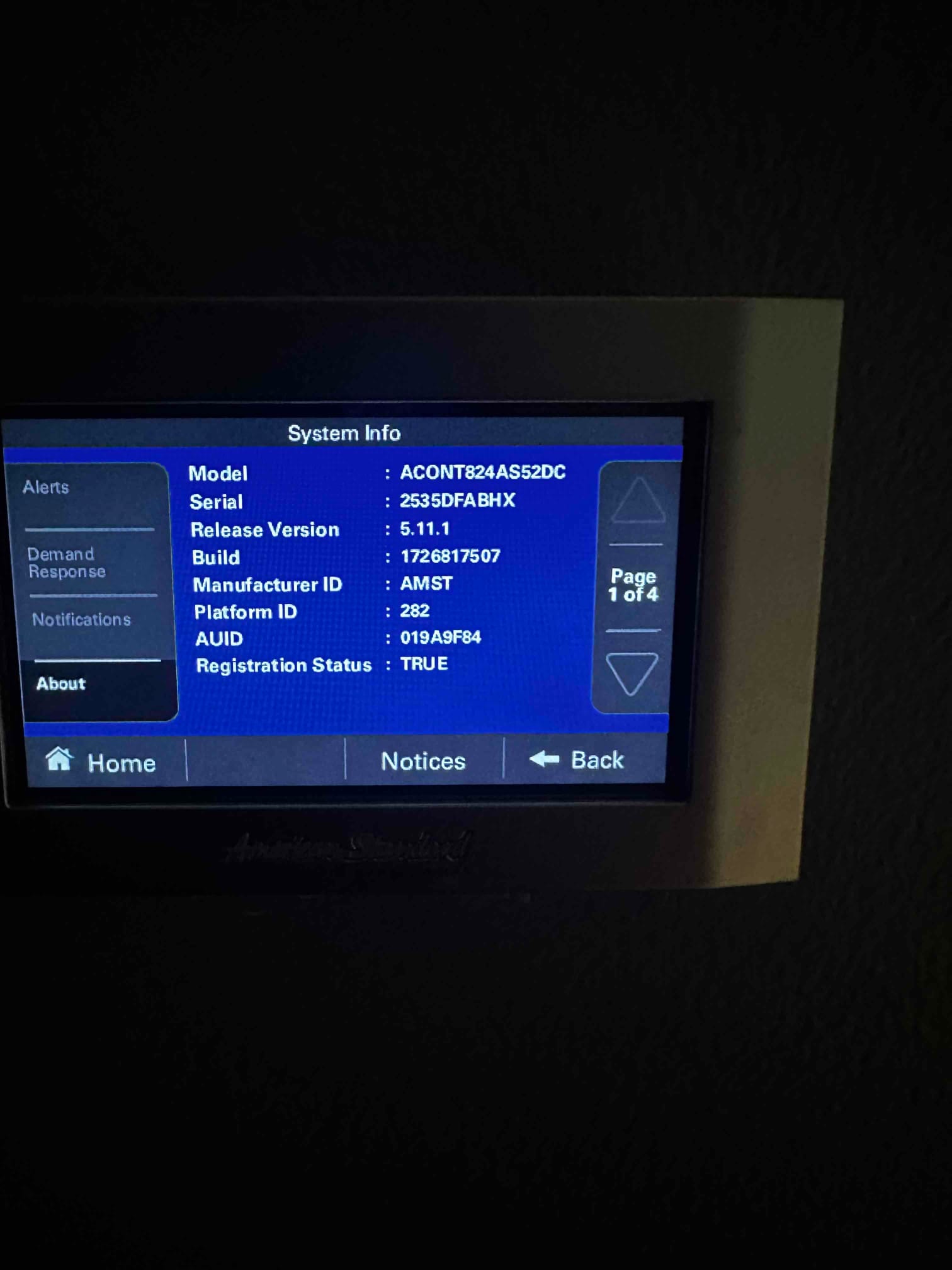Wall-mounted smart thermostat displays system information screen with model, serial, software version, and registration status.