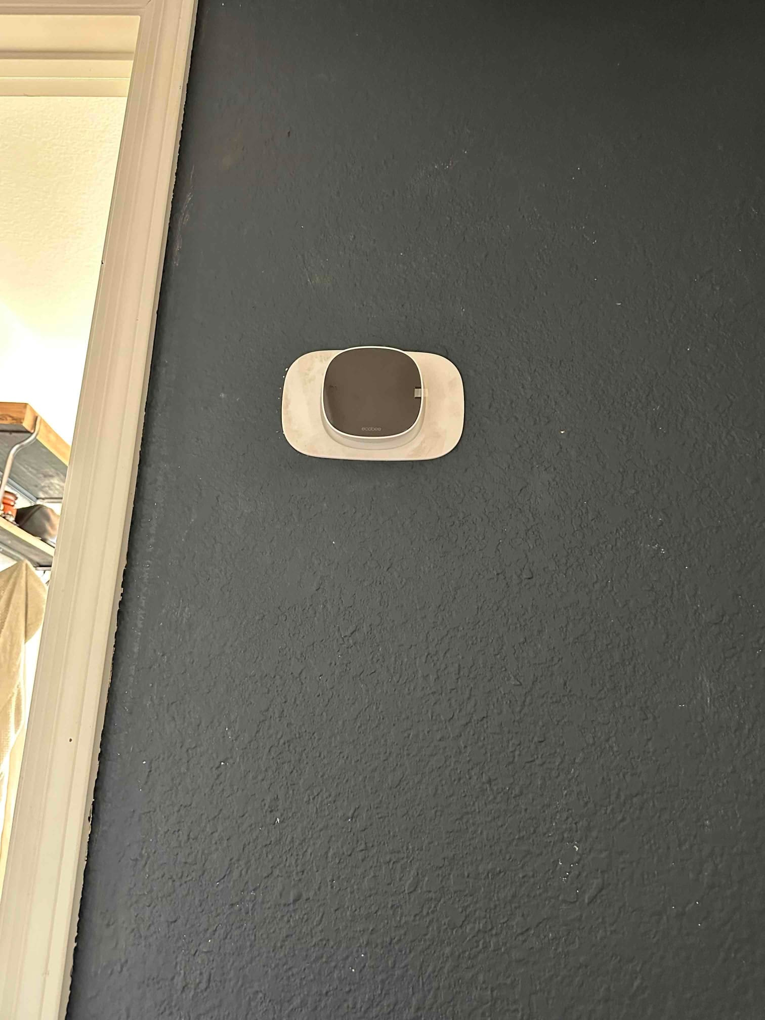 Wall-mounted smart thermostat installed on a finished interior wall with trim visible at the doorway.