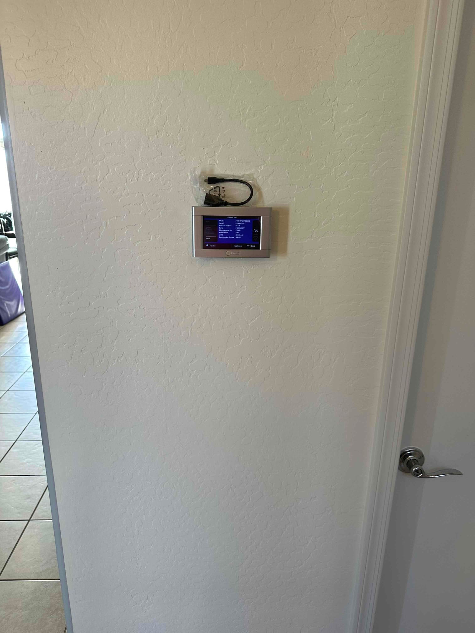 Wall-mounted smart thermostat installed and powered on, displaying system menu and room temperature in a finished hallway.