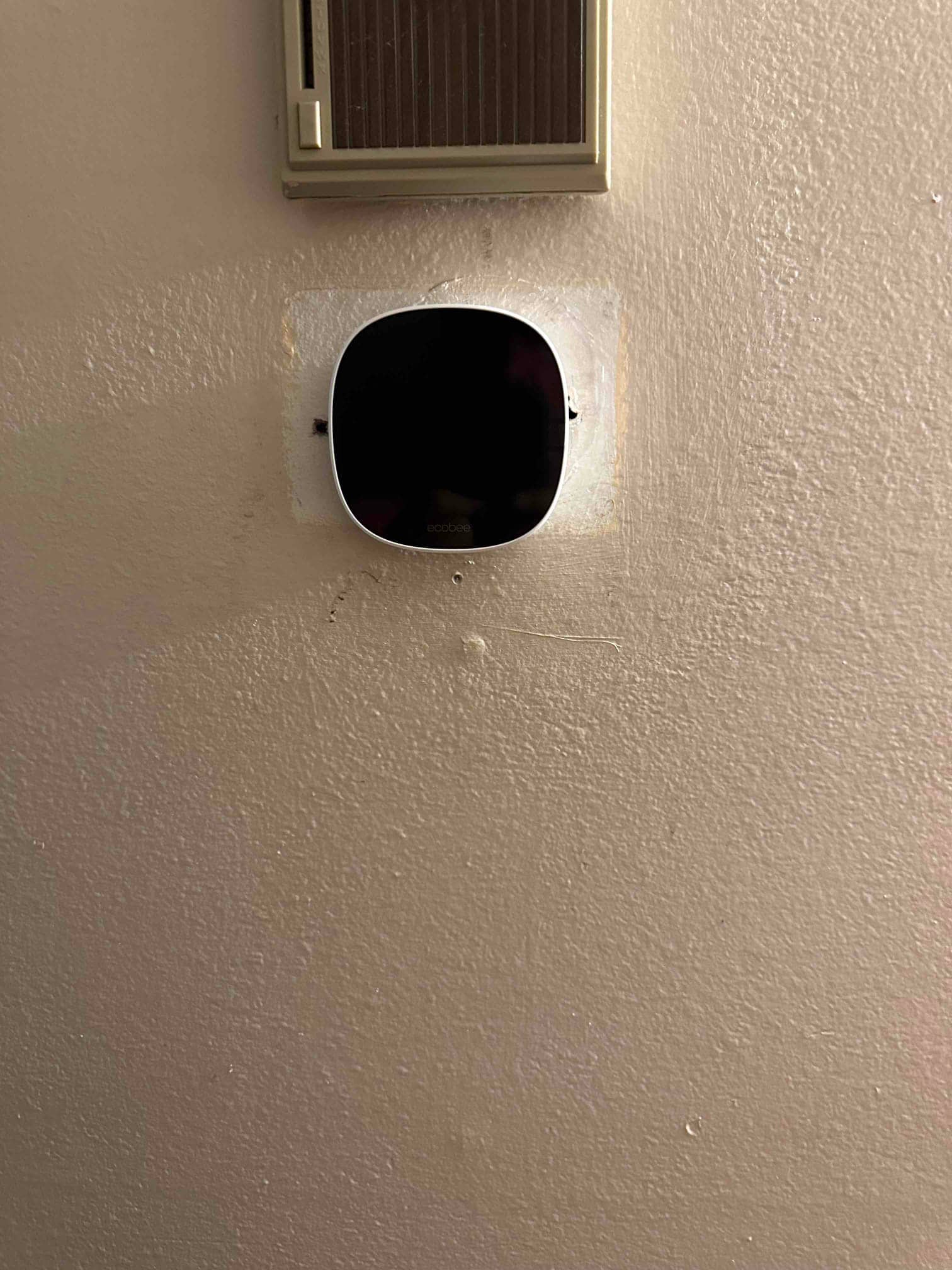 Wall-mounted smart thermostat installed, replacing an older control located just above on the wall.