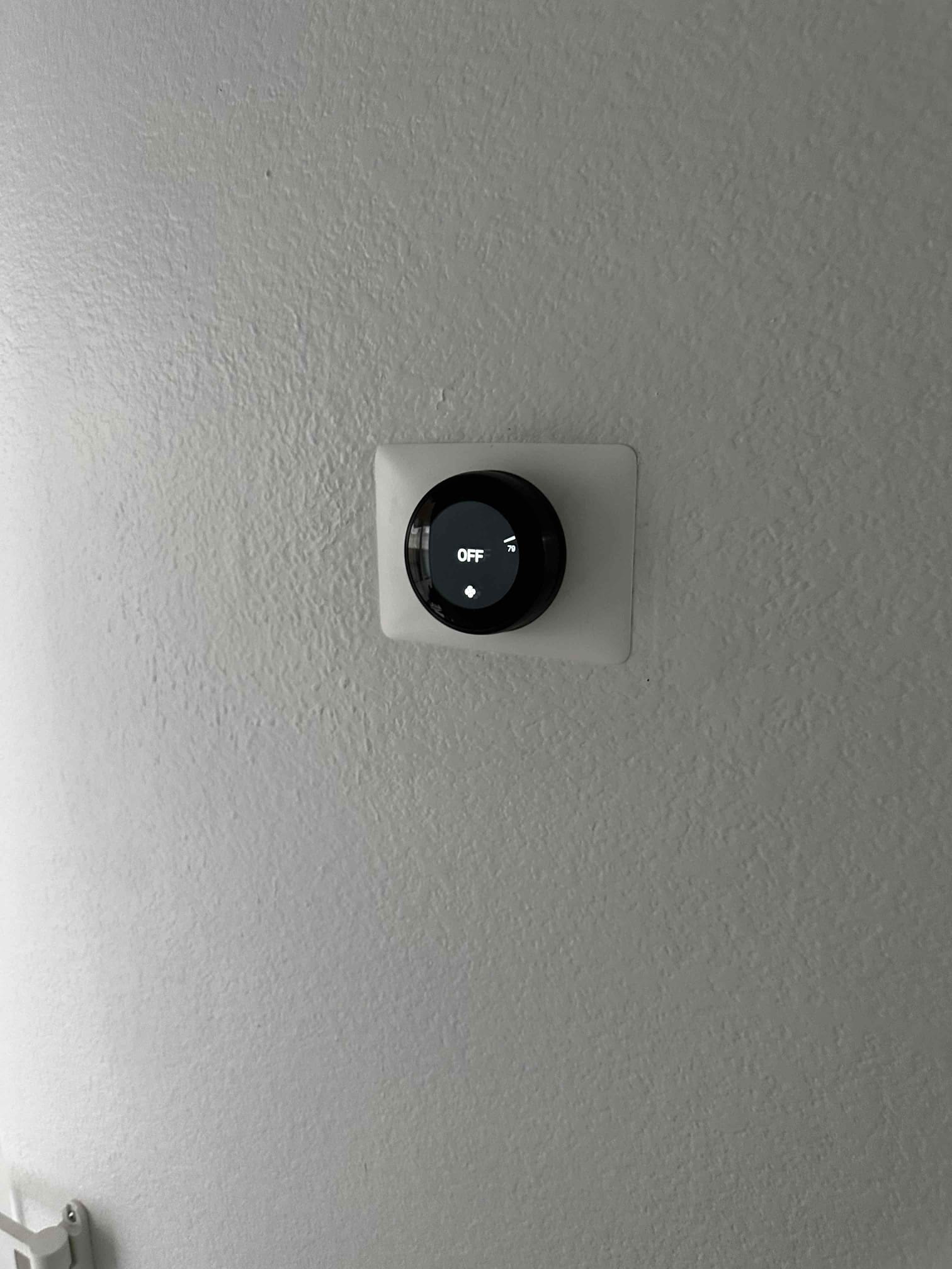 Wall-mounted smart thermostat installed with trim plate, display showing system set to OFF after setup.