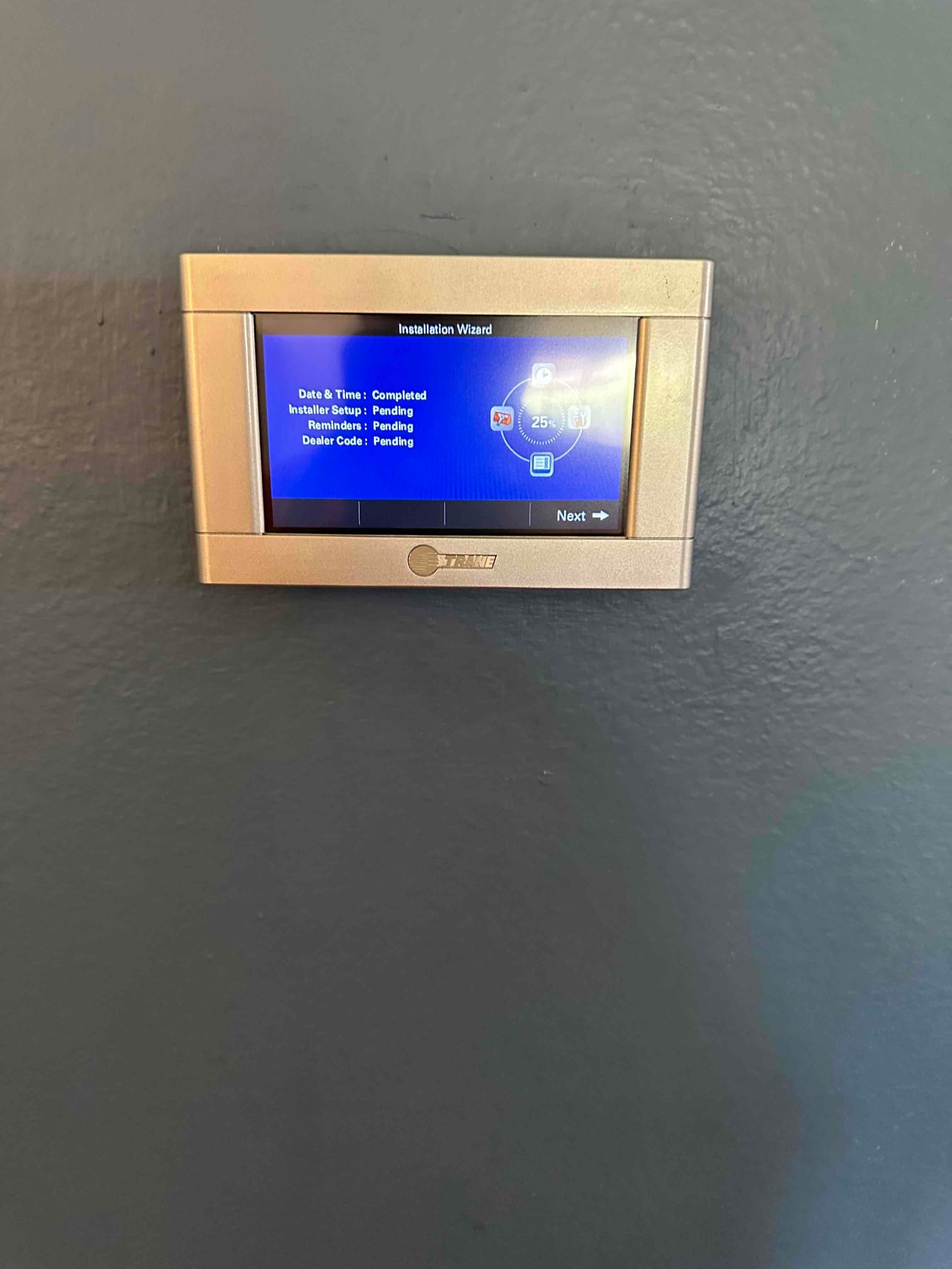 Wall-mounted thermostat displays installation wizard screen with setup items listed and a Next prompt during commissioning.