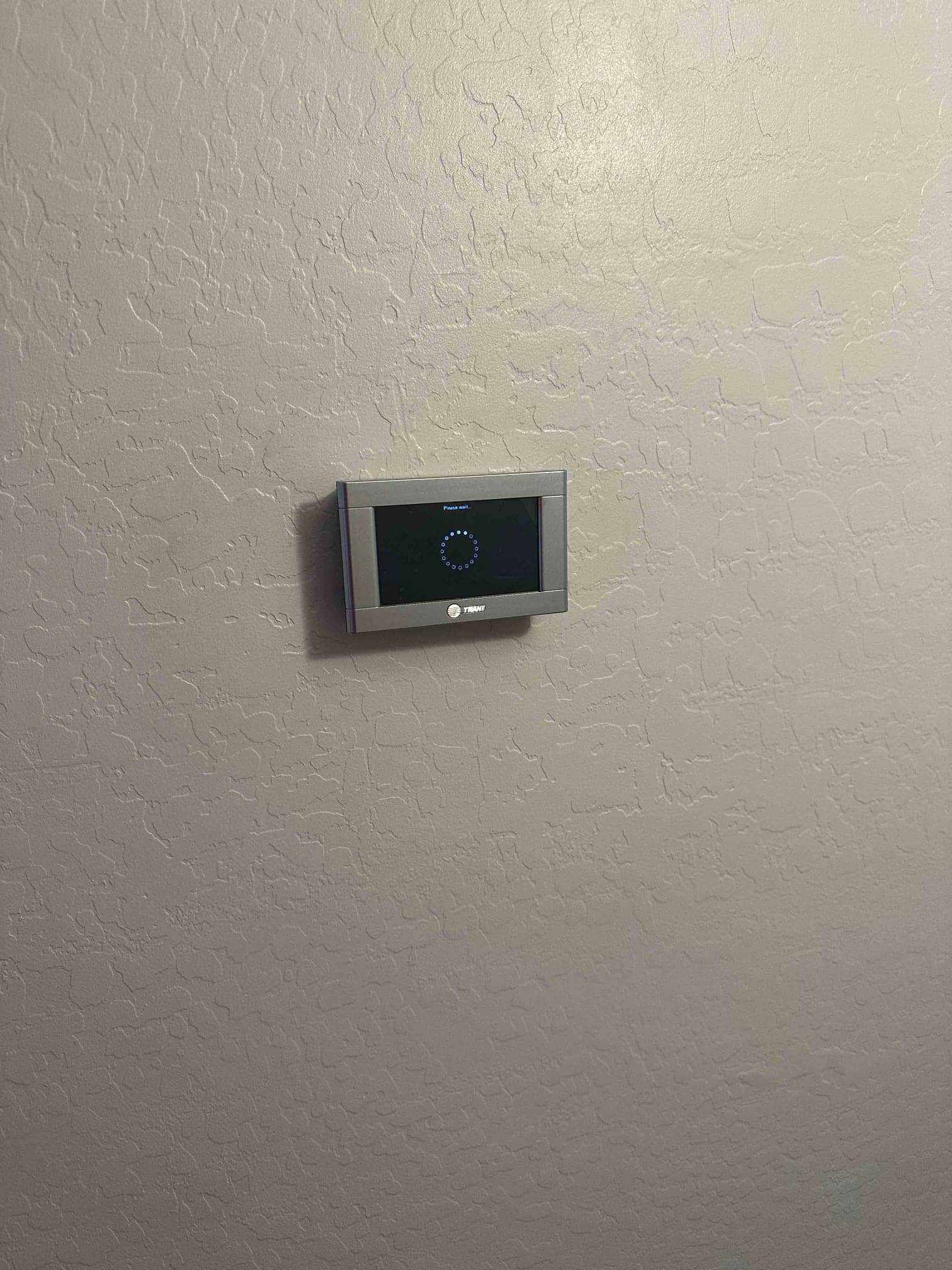 Wall-mounted thermostat installed on finished interior wall, display illuminated and ready for system setup and control.