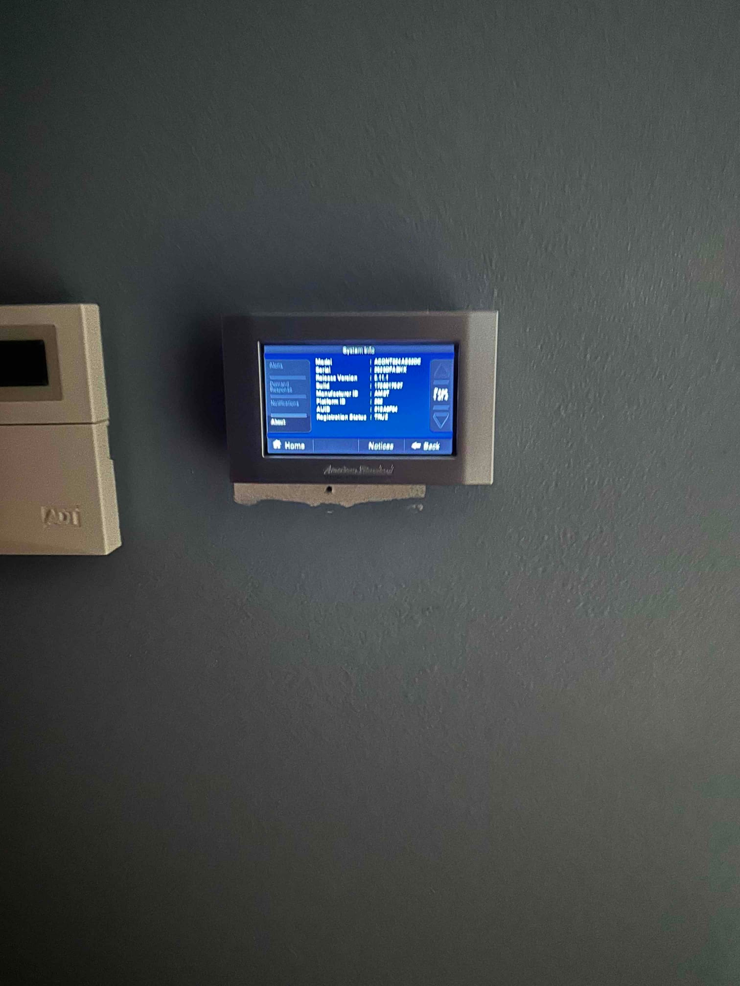 Wall-mounted thermostat installed and powered, displaying system information screen during setup at the indoor location.