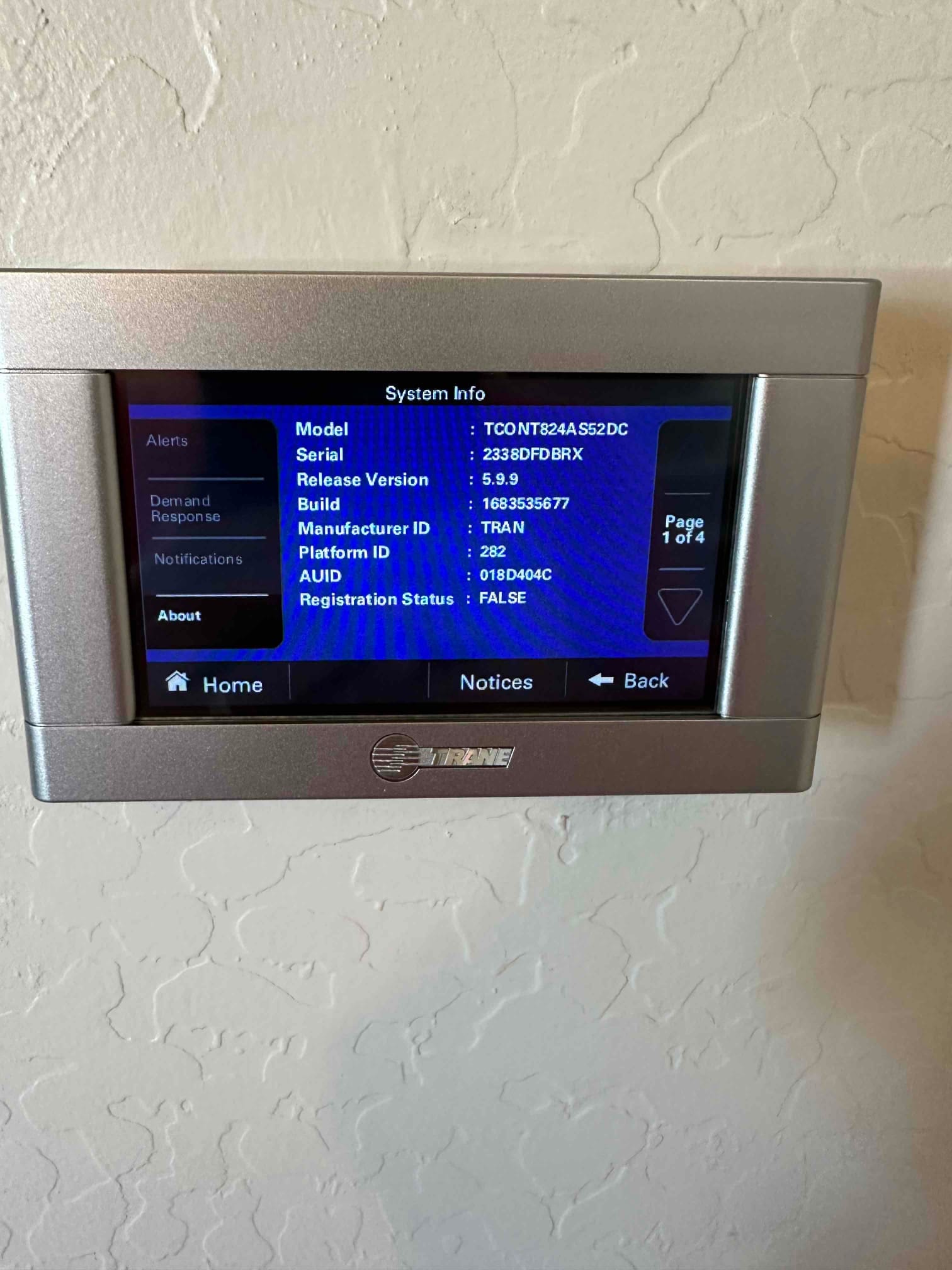 Wall-mounted touchscreen thermostat displays system information on the screen after installation, showing menu options and status details.