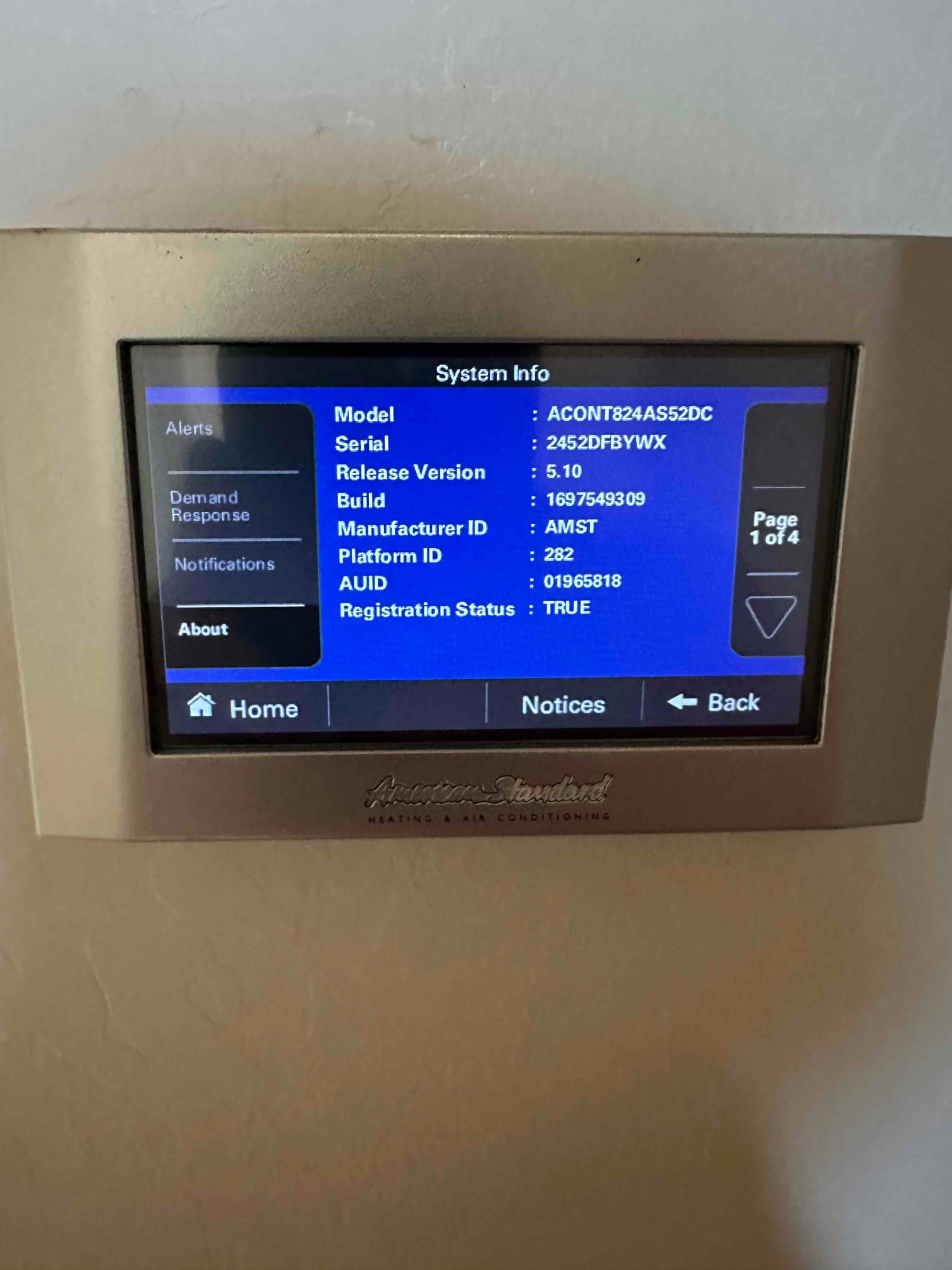 Wall-mounted touchscreen thermostat displays system information menu after installation, showing navigation buttons and on-screen details.