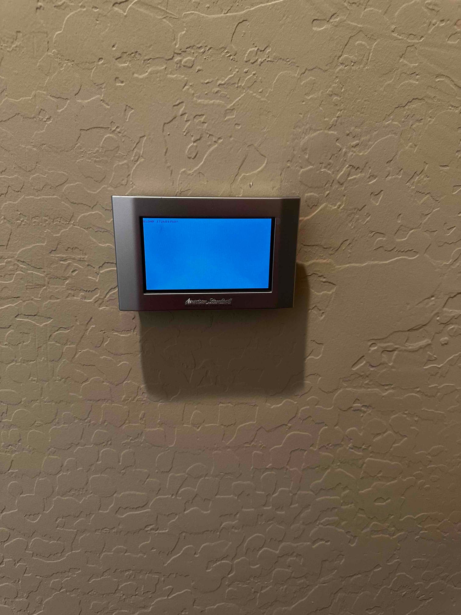 Wall-mounted touchscreen thermostat installed on finished interior wall, screen illuminated and ready for system configuration.