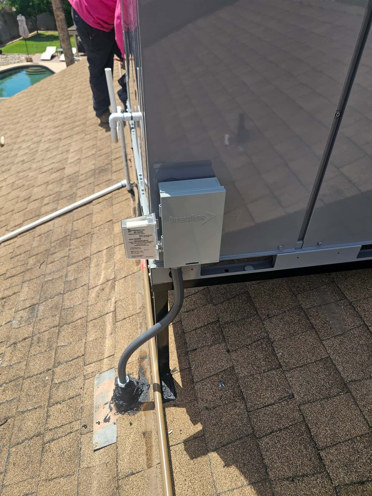 Weatherproof electrical disconnect and flexible conduit installed beside rooftop HVAC unit, with sealed roof penetration and line set support.