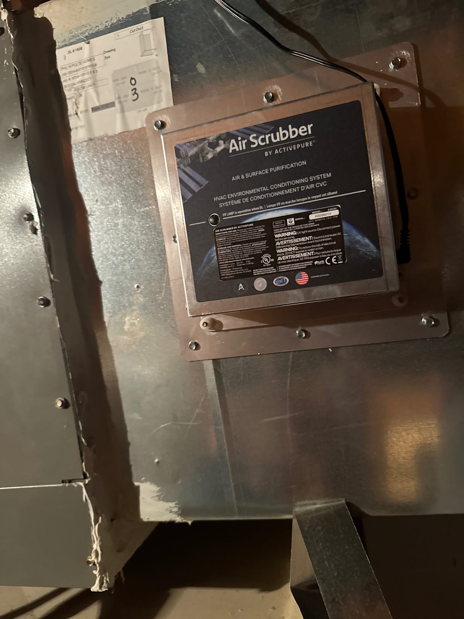 Whole-home ionizing air scrubber installed on ductwork, secured with a mounting plate and visible power connection on the housing.