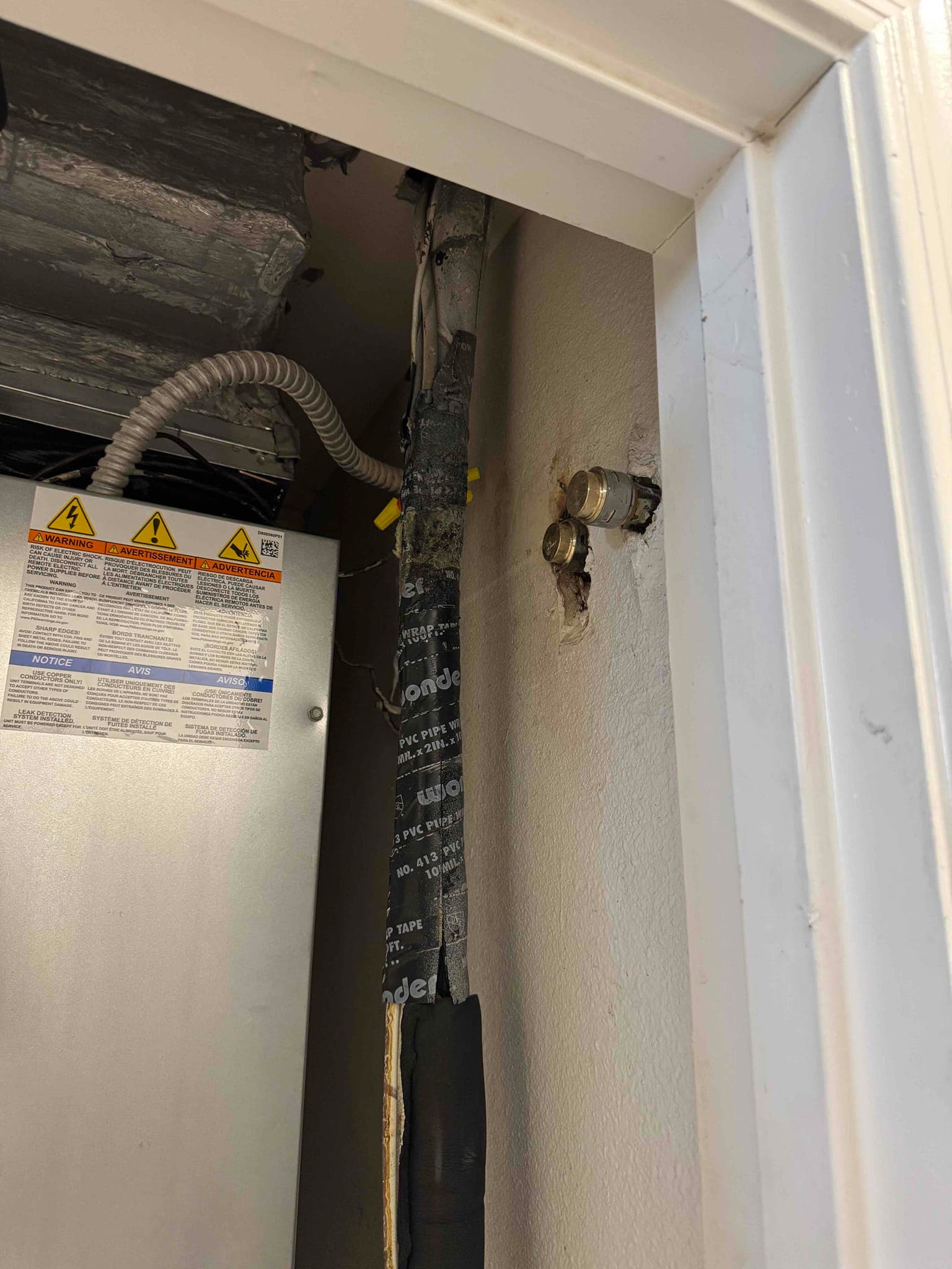 Air handler closet showing secured line set with insulation and electrical whip routing alongside wall penetration fittings.