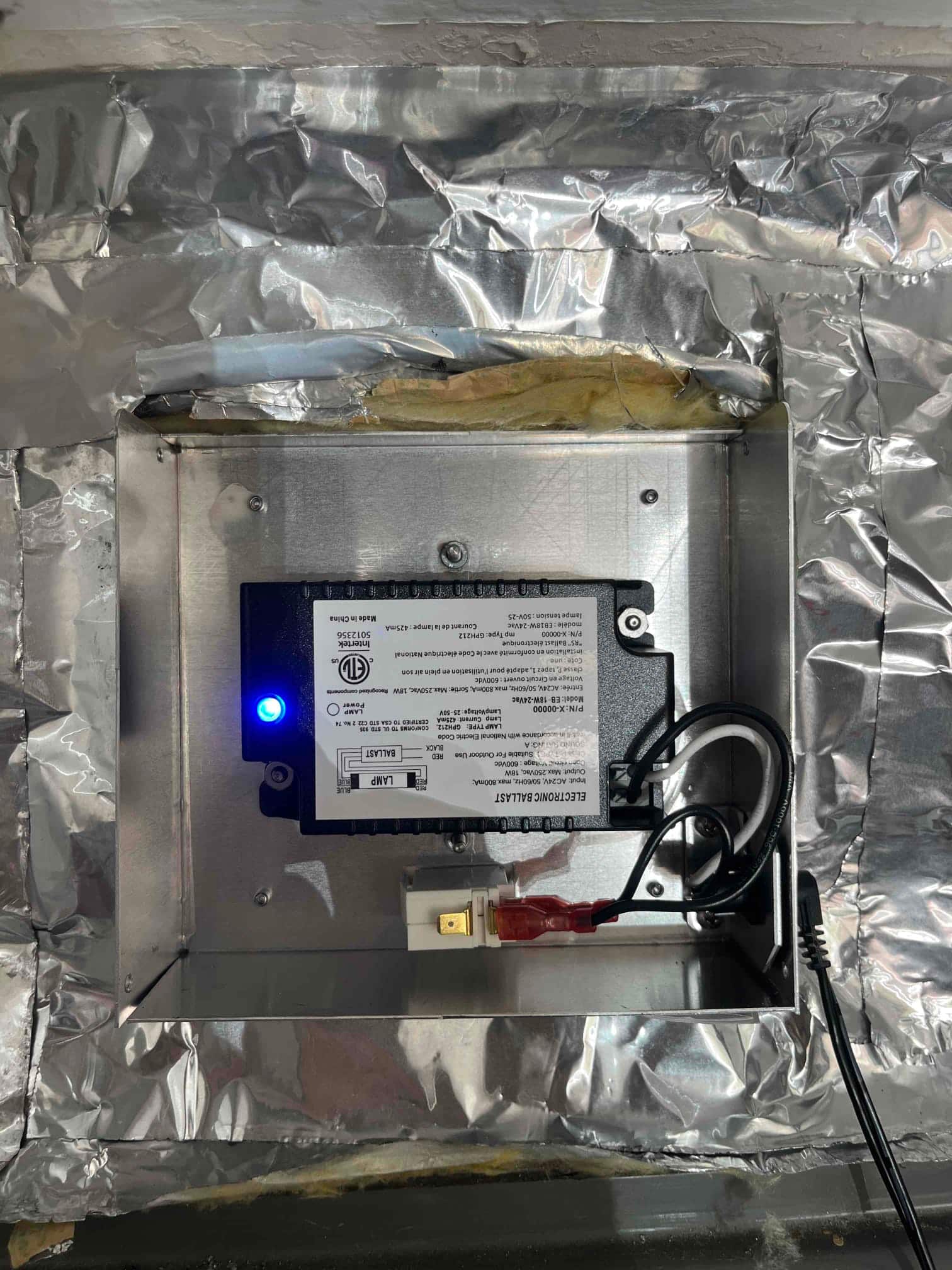 Air scrubber control module installed inside a metal plenum box, blue status LED illuminated and wiring connected.