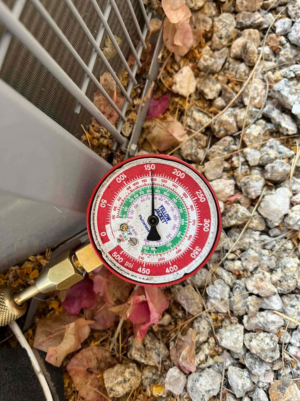 Analog manifold gauge connected at the outdoor unit shows low-side pressure at approximately 65 psi during system diagnosis.