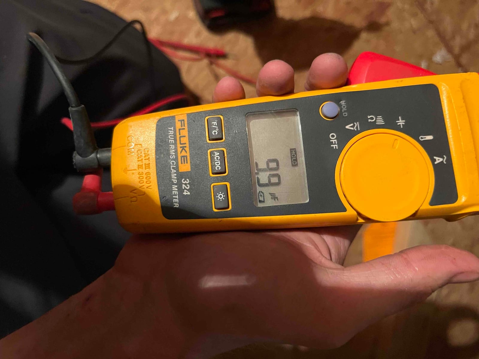 Clamp meter display shows 9.9 A while measuring current with the clamp around a conductor.