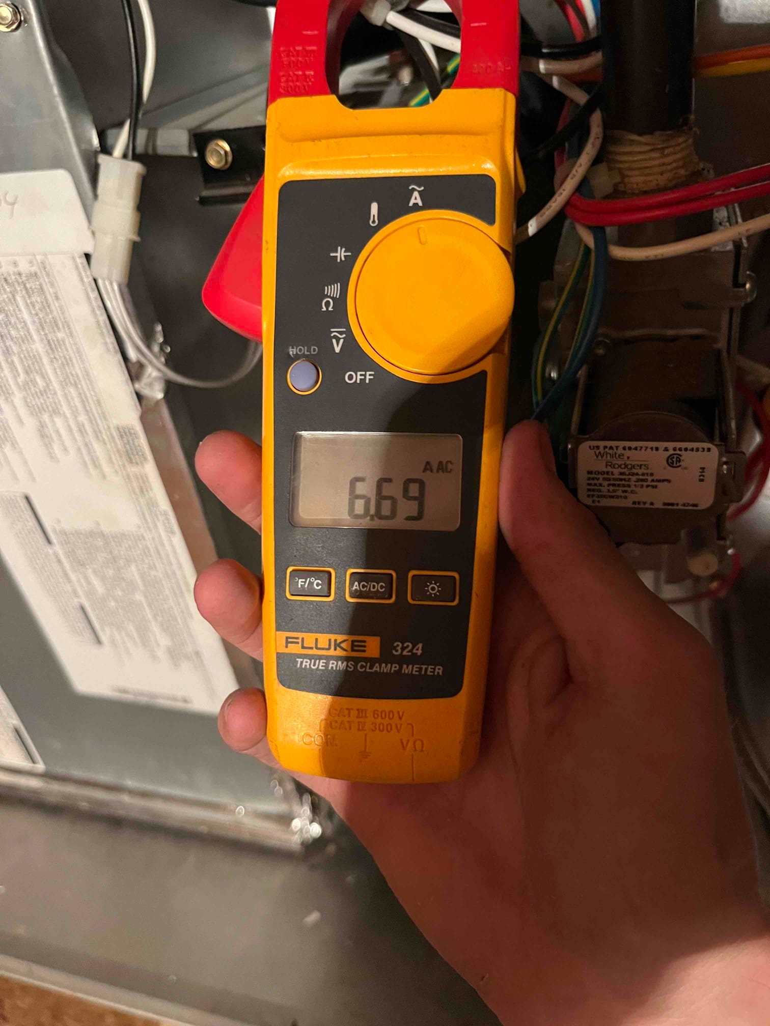 Clamp meter displays 6.69 A AC with jaws around a single conductor inside the air handler compartment.