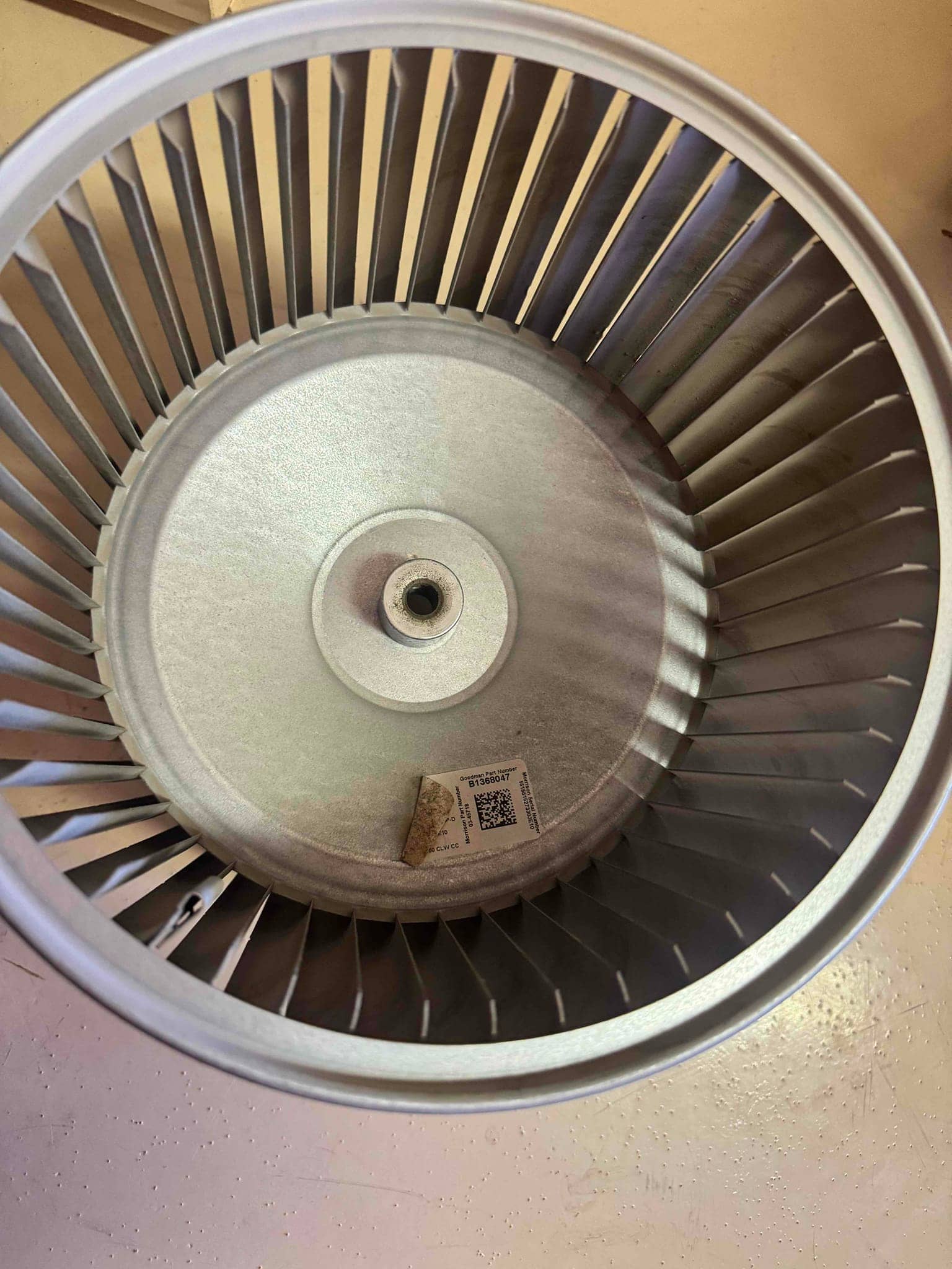 Cleaned blower wheel removed from the air handler, showing intact fins and a QR-labeled tag inside the housing.
