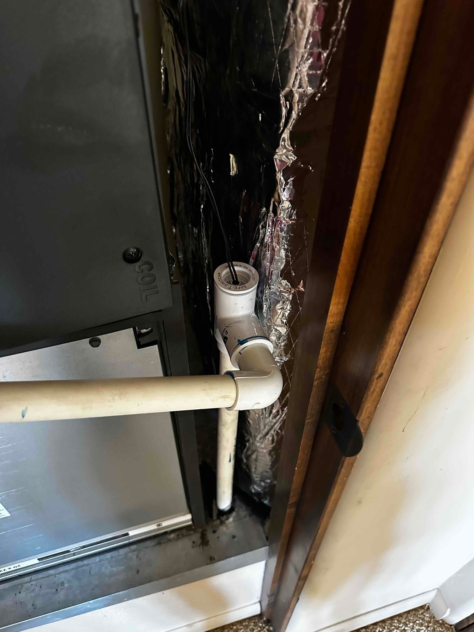 Condensate drain assembly at the air handler with a cleanout tee and float switch wiring visible at the trap.