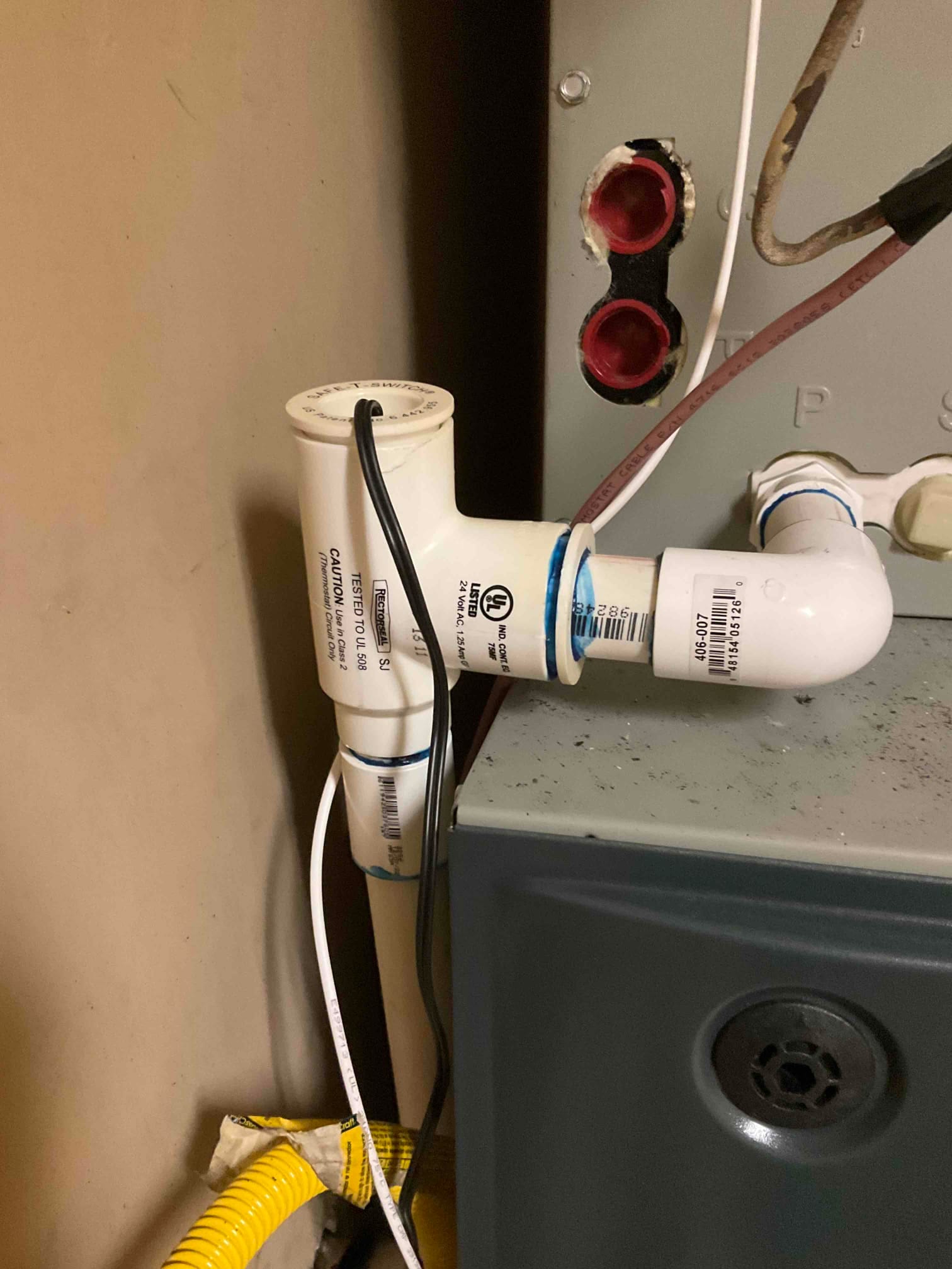 Condensate drain assembly with cleanout and trap connected to the indoor unit, with low-voltage control wires routed alongside.