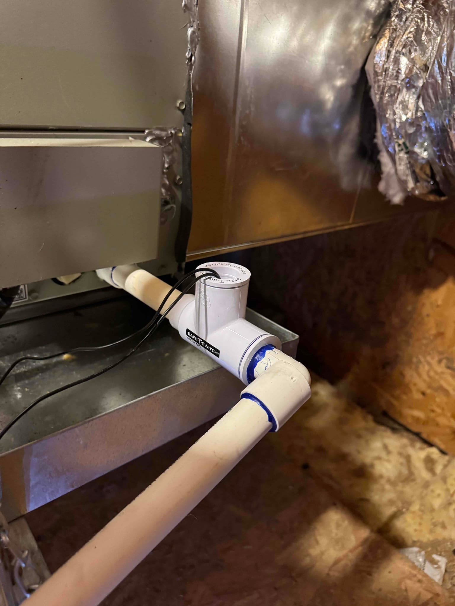 Condensate drain assembly with inline float safety switch installed at the air handler drain connection, glued PVC fittings, and wiring routed.