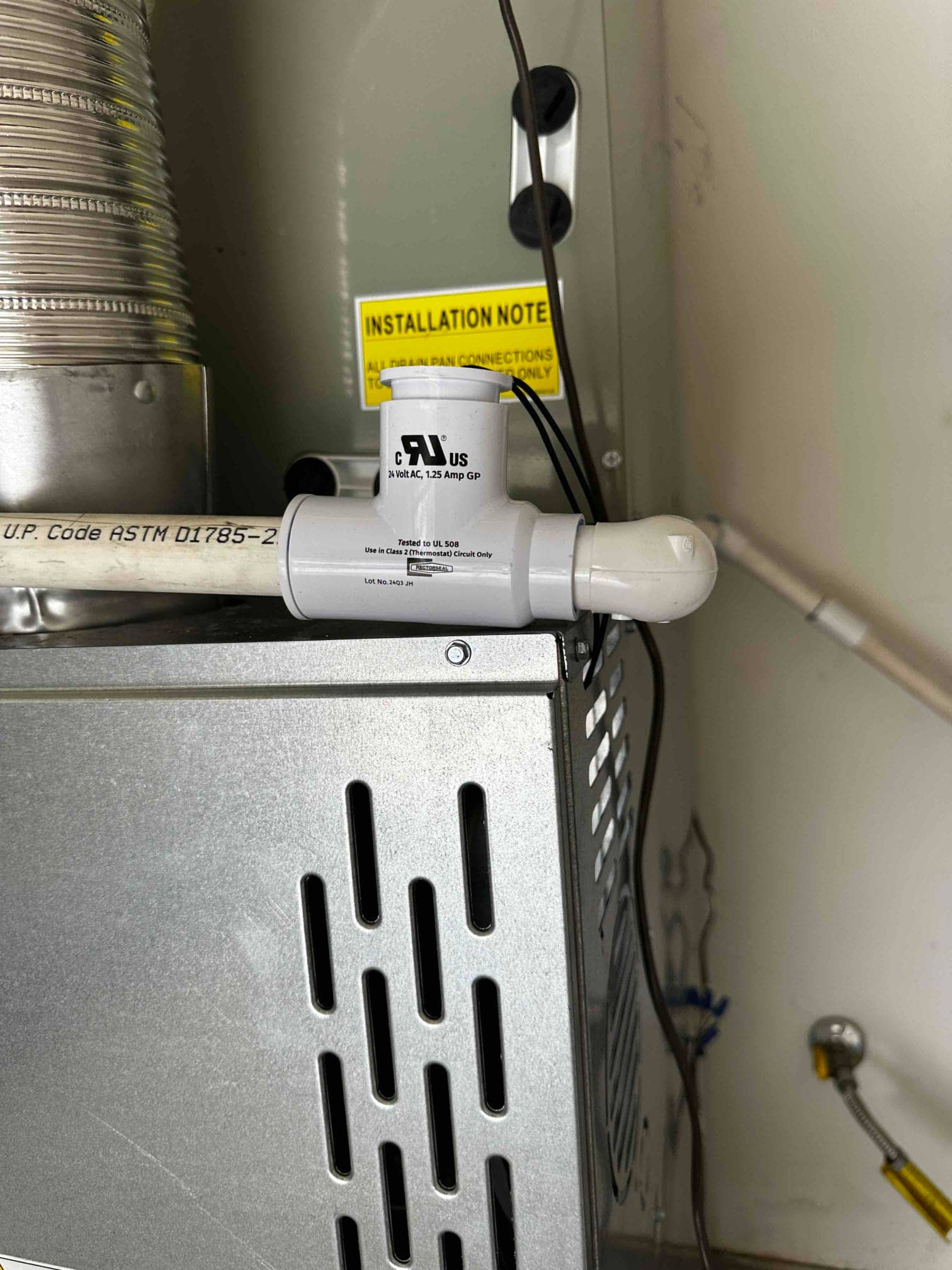 Condensate drain with float safety switch installed on the furnace, with venting and cabinet visible during the HVAC installation.